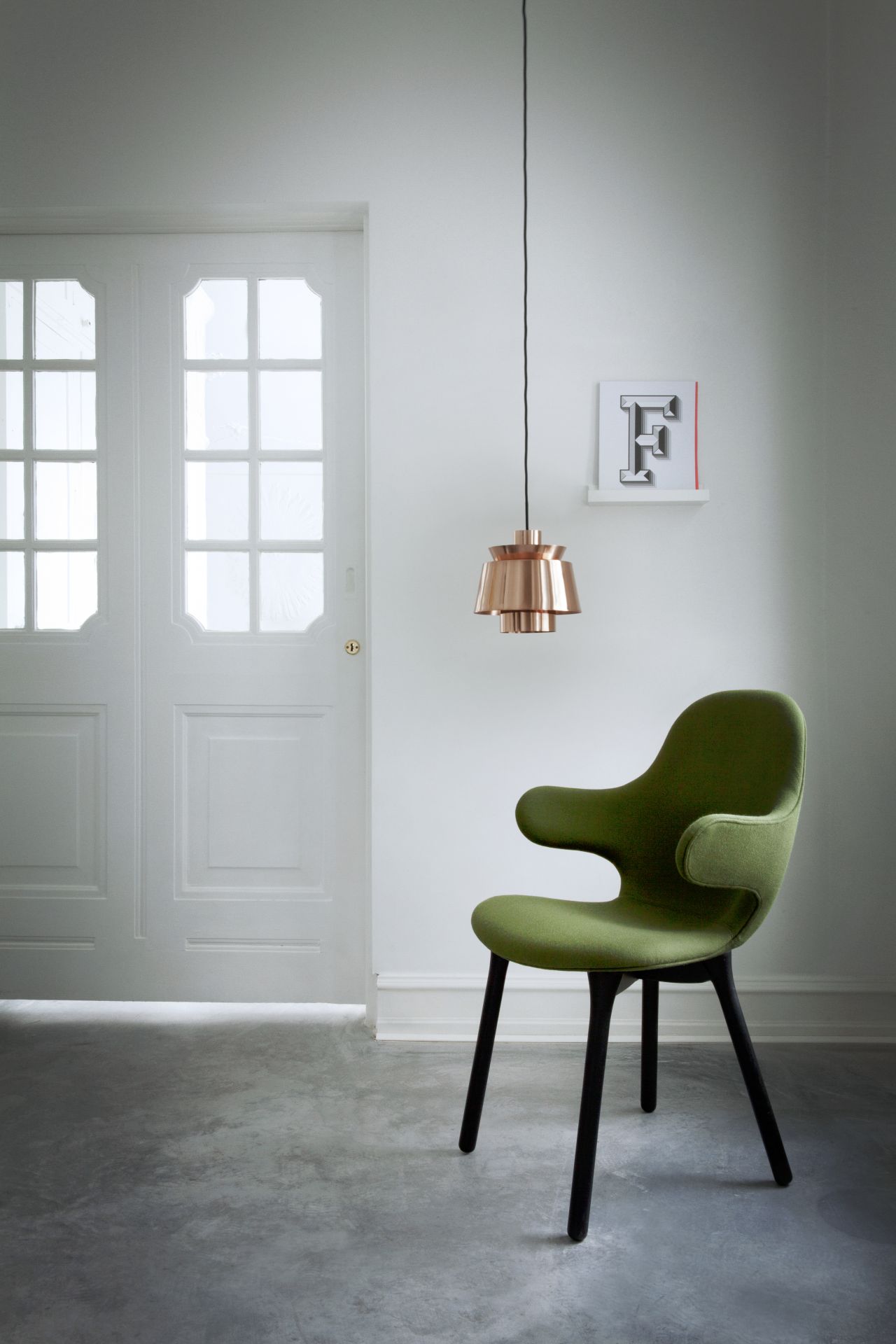 AndTradition Catch Chair JH1 Stuhl in Grün mit schwarzen Beinen vor weißer Tür und Lampe.