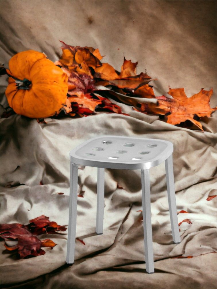 Silberner Emeco 1 Inch Aluminium Hocker mit Löchern auf beigem Stoff mit Herbstdeko.