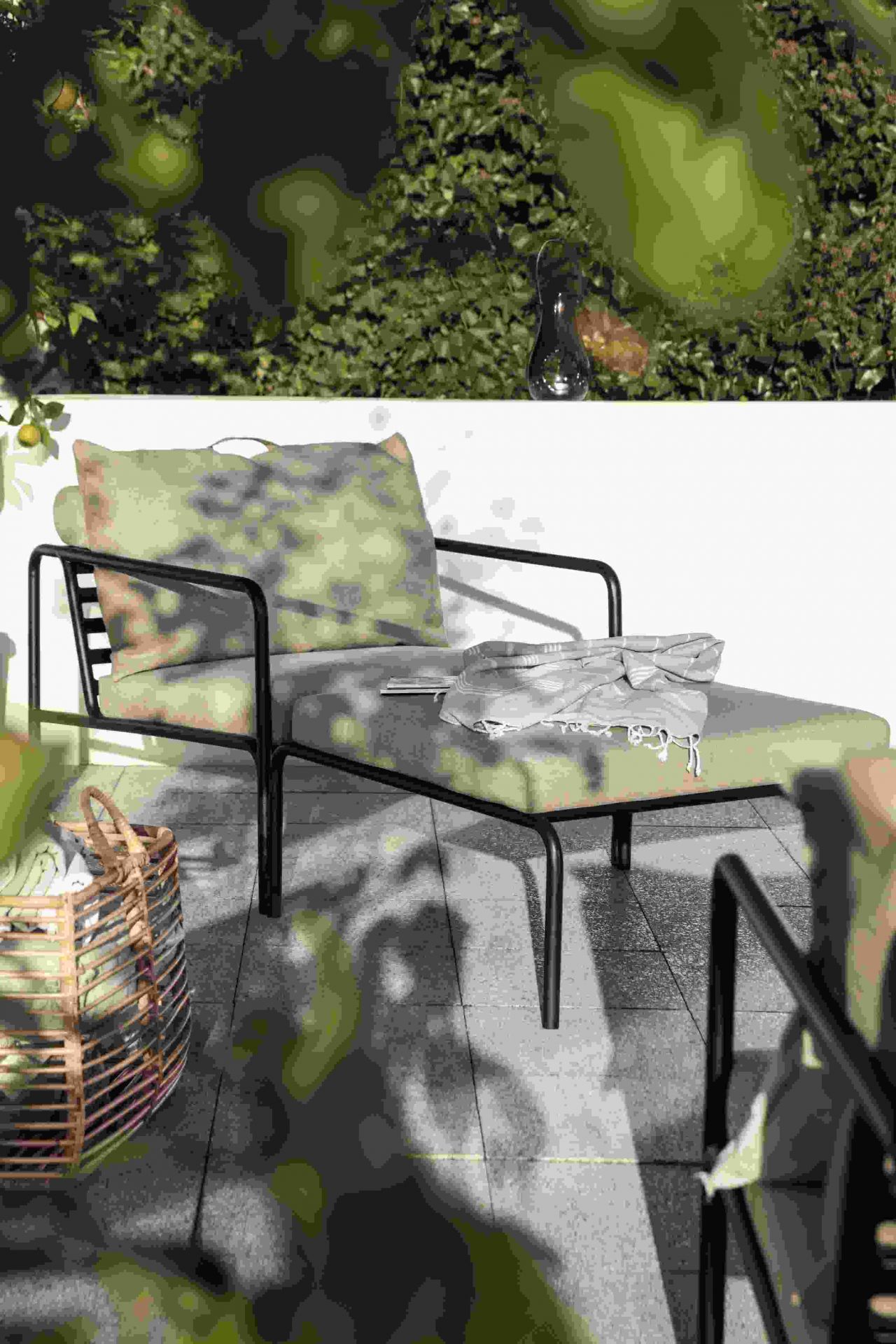 Avon Ottoman Outdoor Hocker mit Kissen und Decke auf einer Terrasse im Garten.