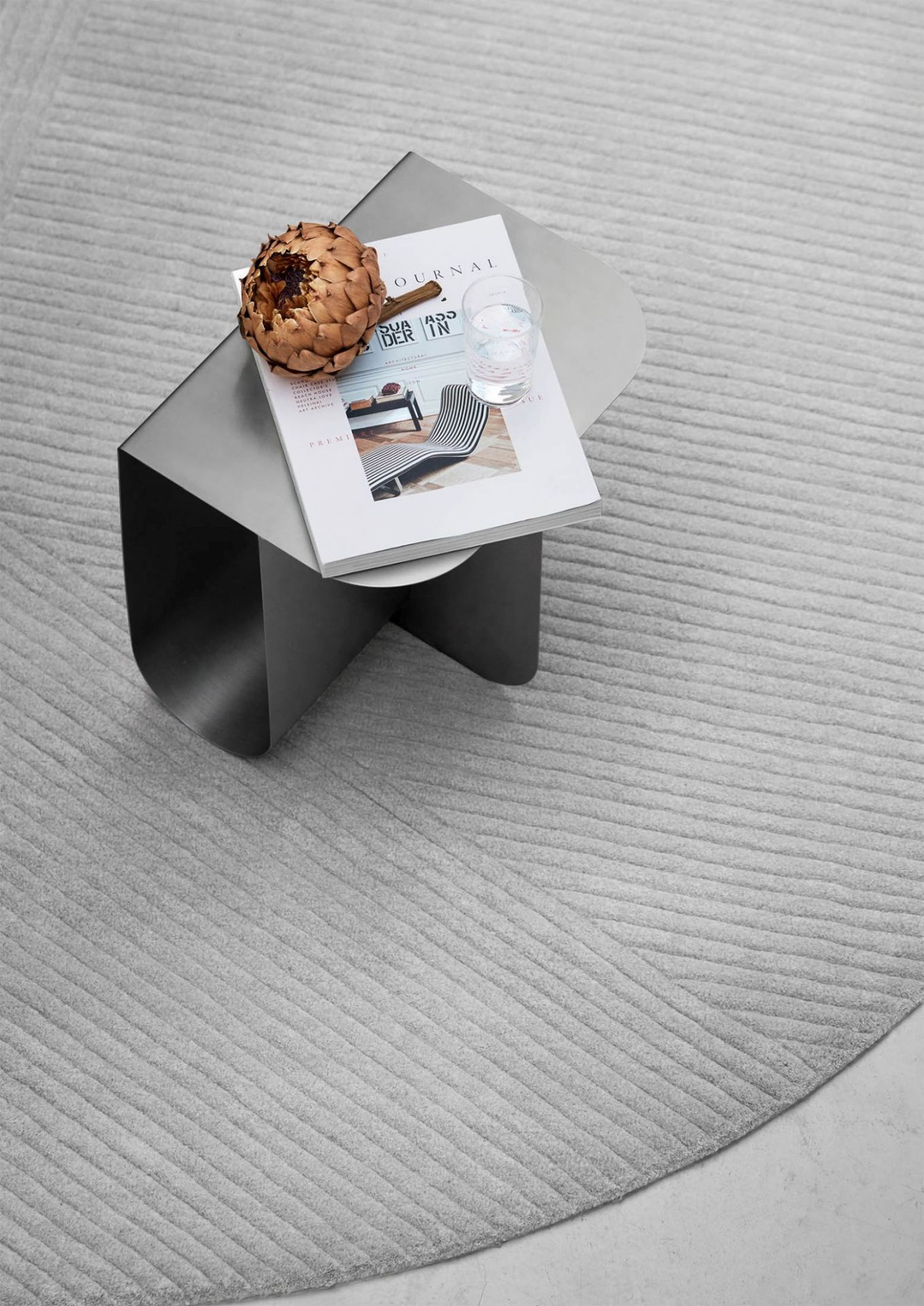 Mass Beistelltisch aus Stahl von Northern, modernes Design mit Magazin, Wasserglas und Artischocke auf grauem Teppich.