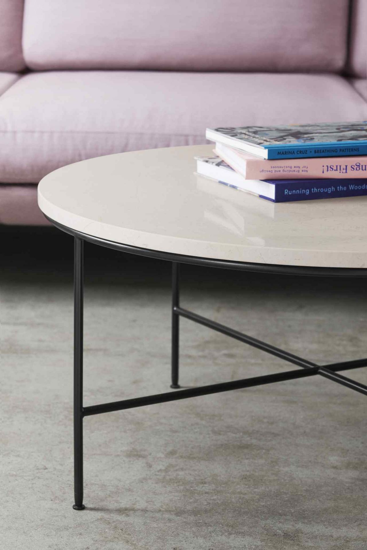 Detailaufnahme eines runden Couchtisches mit schwarzem Metallgestell und Büchern, im Hintergrund ein Fritz Hansen Sofa.