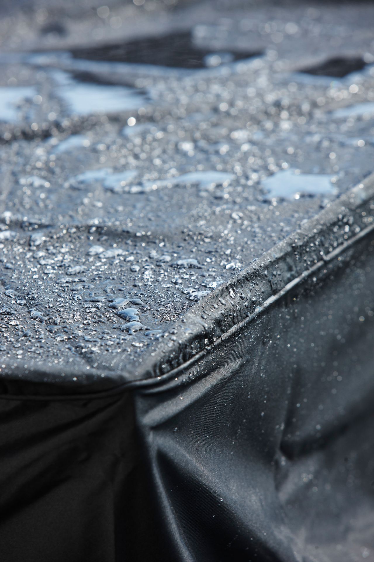 Detailaufnahme einer schwarzen Cane-Line Schutzhülle für Gartenmöbel, bedeckt mit Wassertropfen, die ihre Wasserdichtigkeit demonstrieren.