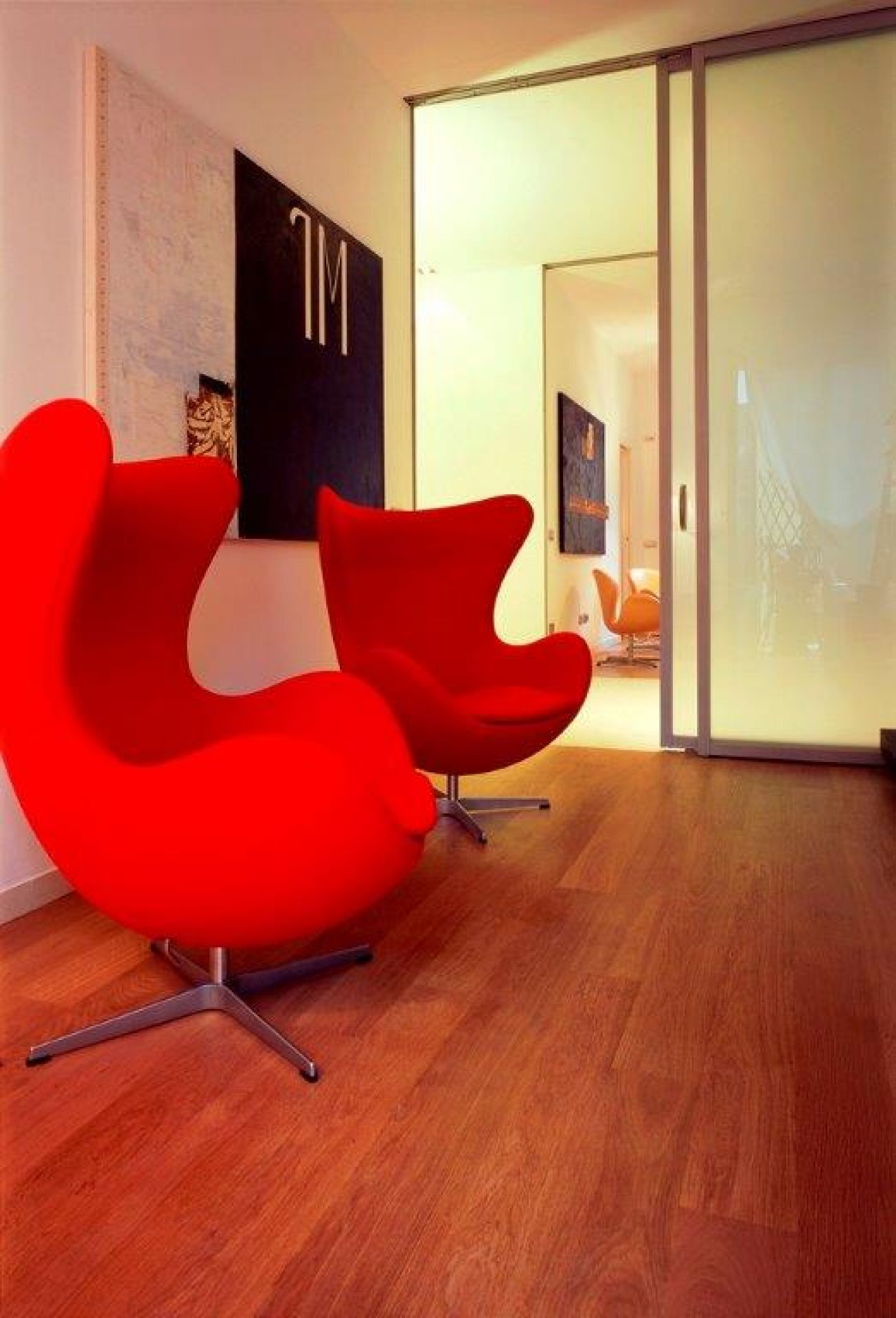 Zwei rote "Das Ei" Sessel von Fritz Hansen auf einem Holzboden in einem modernen Interieur.