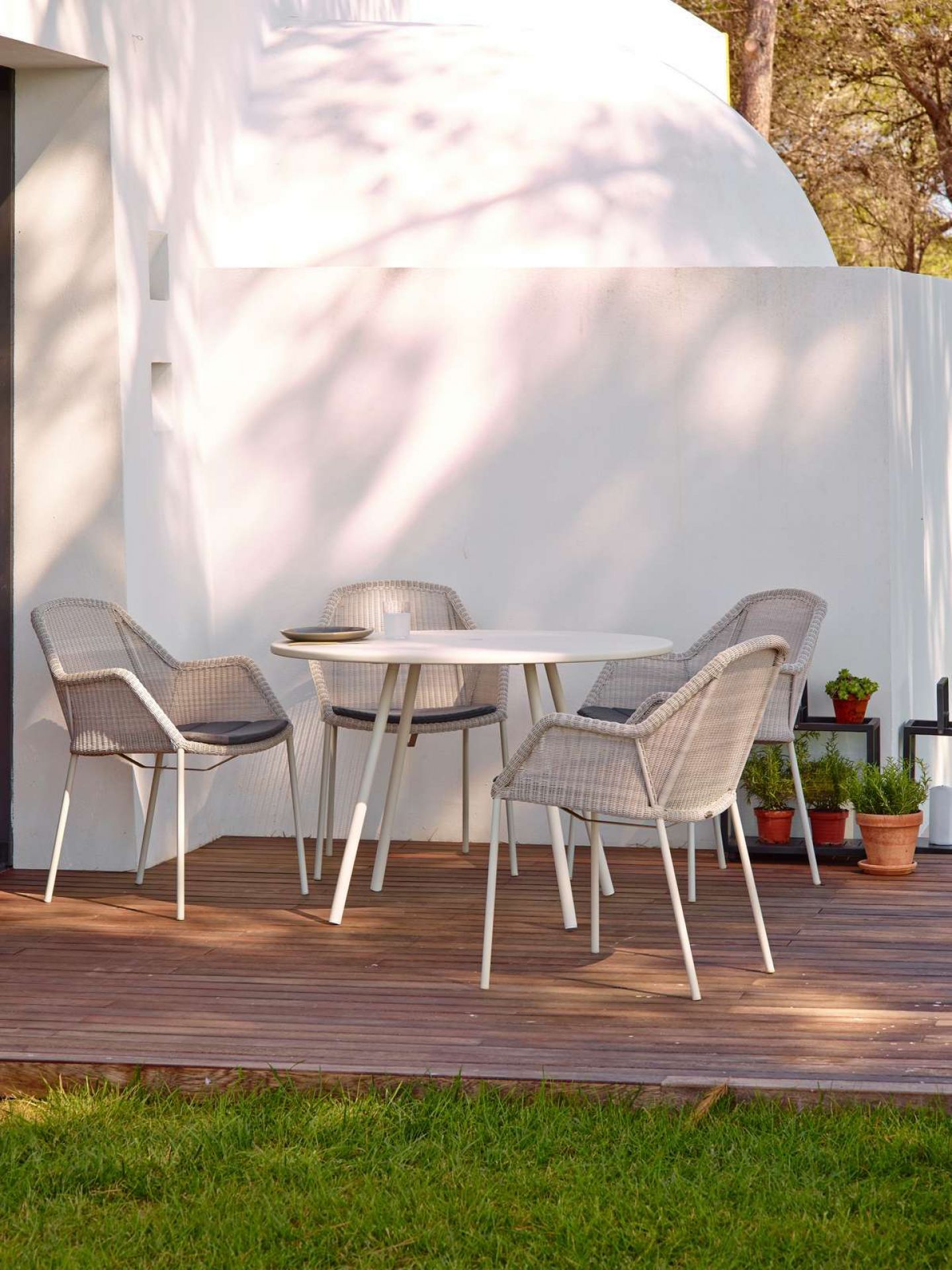 Breeze Outdoor Stühle von Cane-Line mit Vierfußgestell und grauem Geflecht um einen runden Gartentisch.