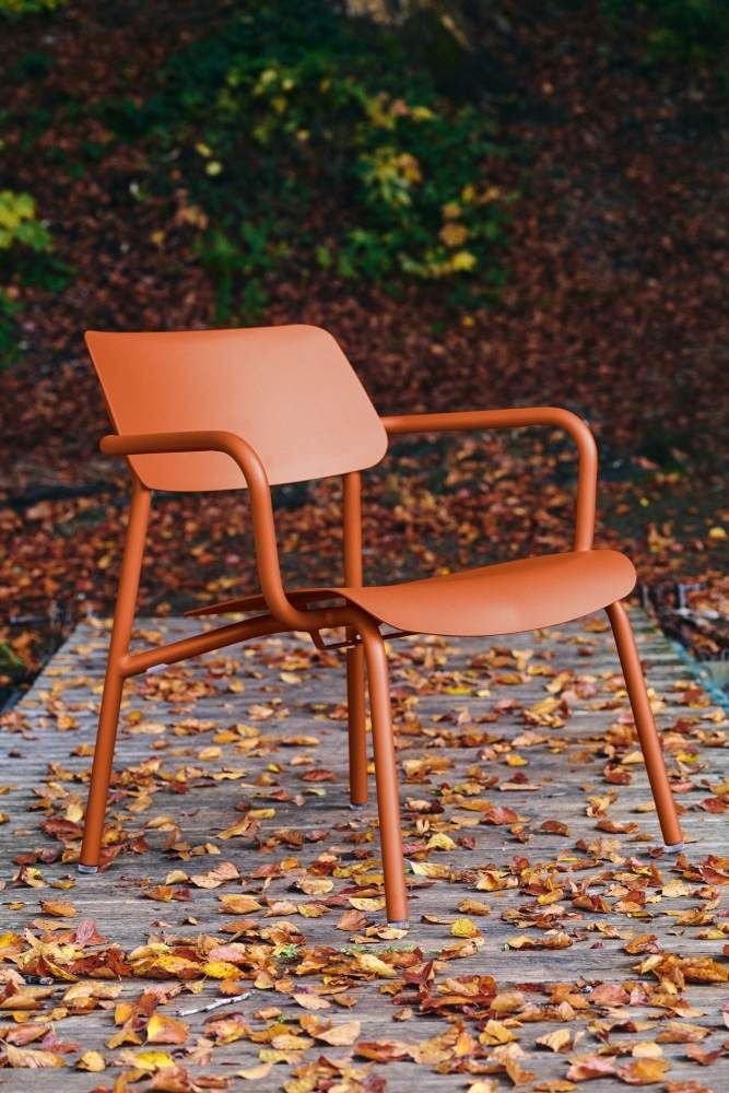 Nahaufnahme des orangefarbenen Fermob Studie Lounge Sessels Outdoor auf einem Holzsteg mit Herbstlaub.