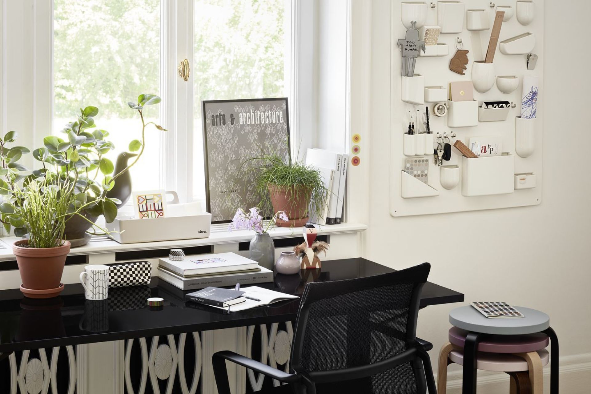 Detailaufnahme eines Schreibtisches mit Vitra Holzfigur, Pflanzen, Büchern und einem Wandorganizer im hellen Arbeitszimmer.
