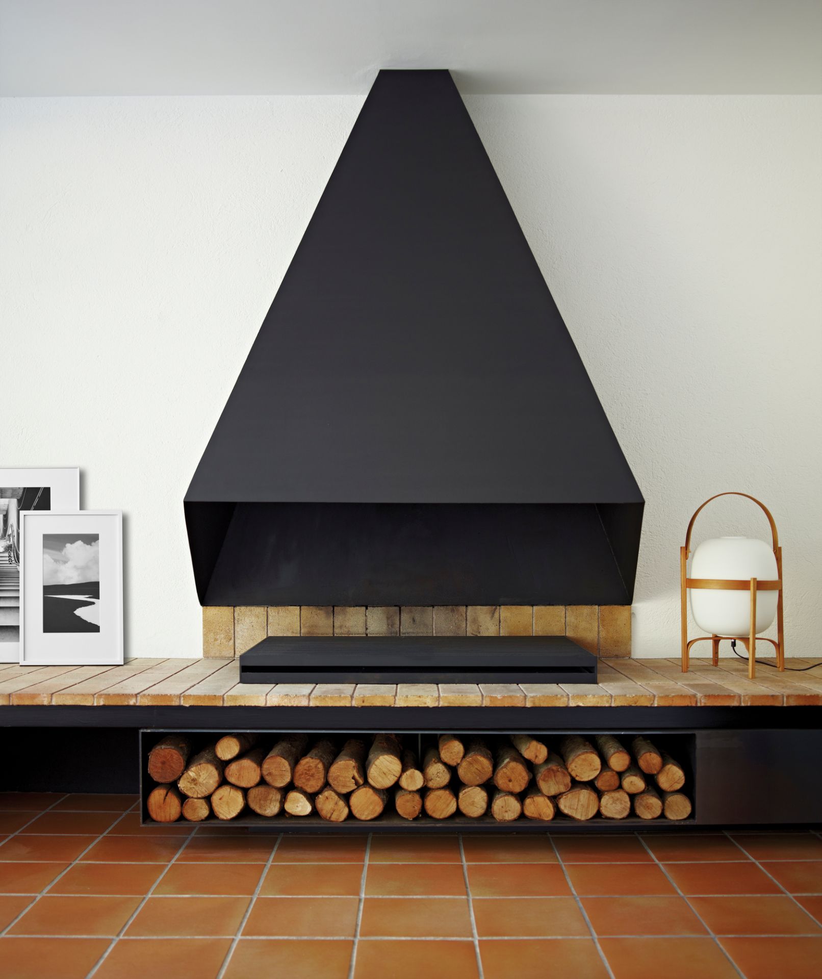 Cesta Tischleuchte von Santa & Cole als Nachttischlampe neben Kamin mit Holzscheiten im Wohnzimmer.