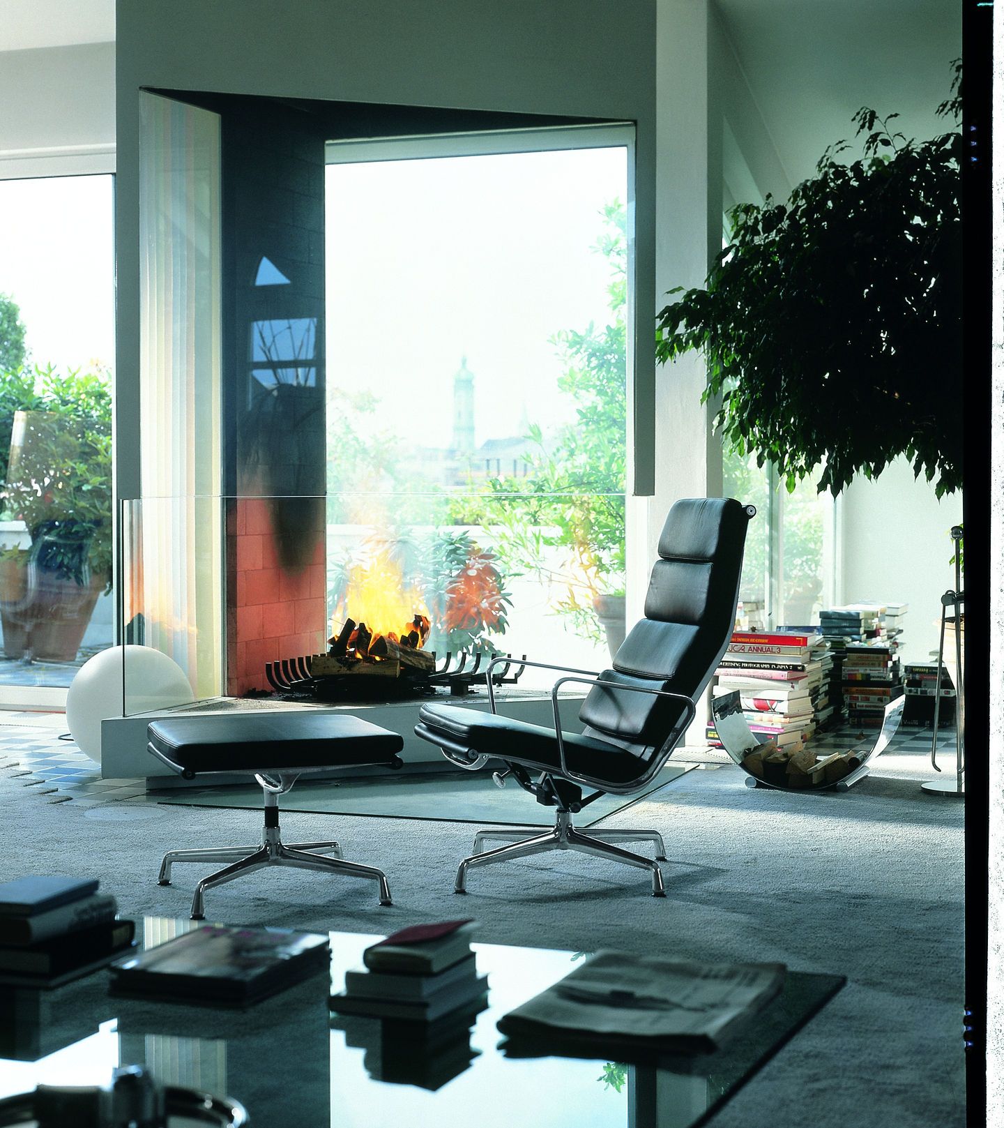 Schwarzer Vitra Soft Pad Chair EA222 mit Hocker vor Kamin und Fenster für entspanntes Wohnen.