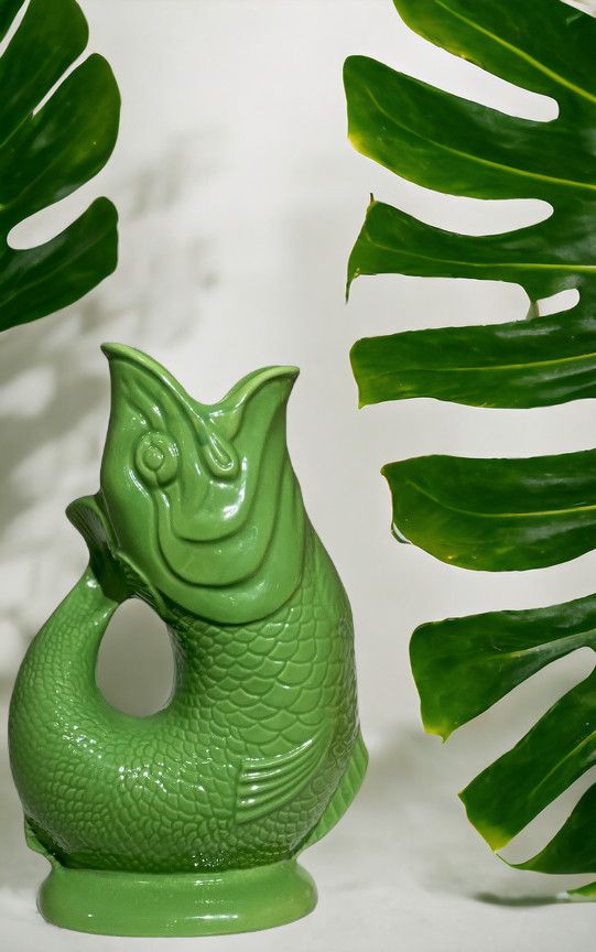 Grüne Gluckigluck Fischkaraffe, XL, in Apfelgrün, neben tropischen Blättern. Dekorative Keramikvase in Fischform.