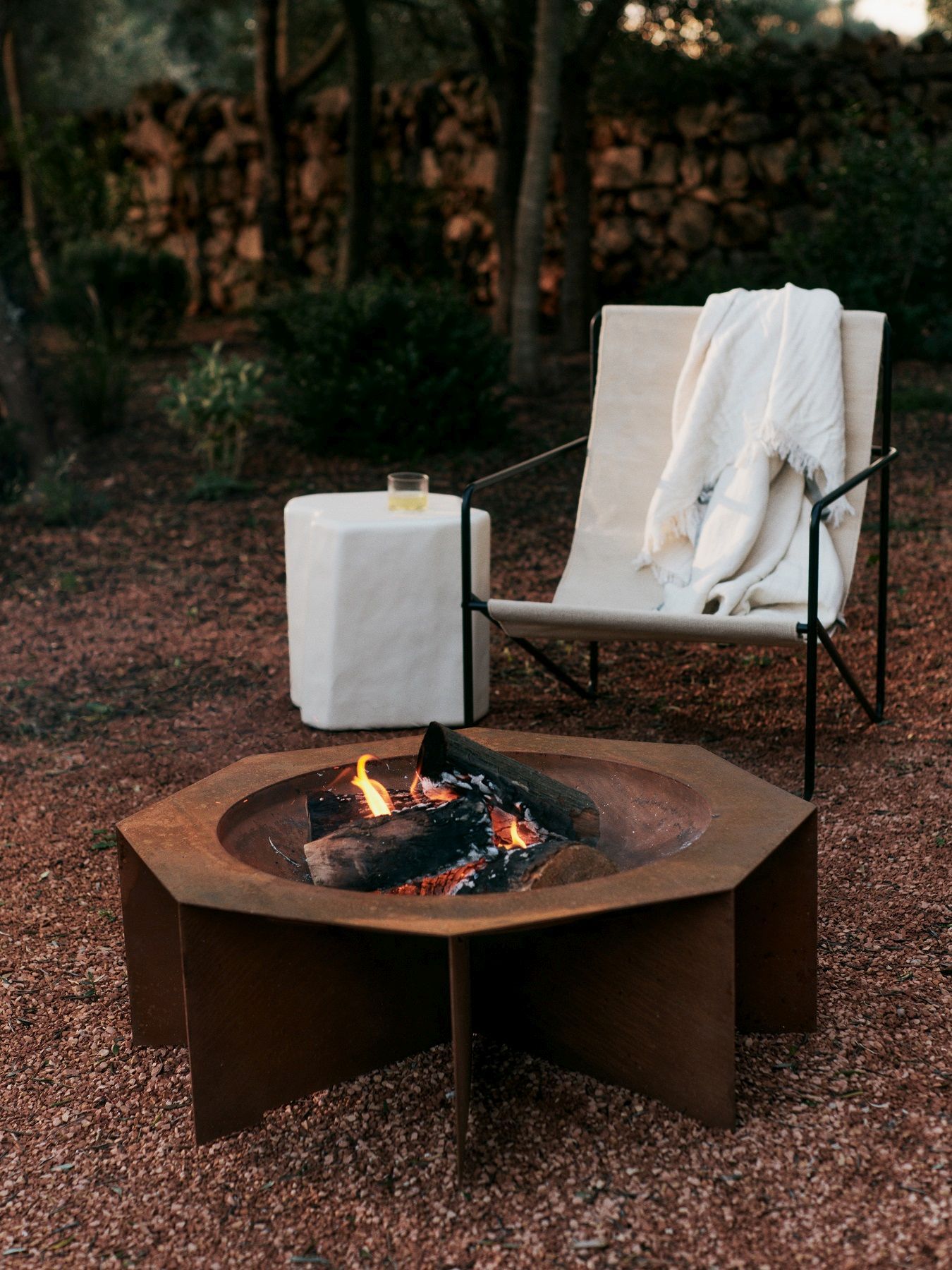 Desert Chair Loungesessel von Ferm Living mit Feuerstelle und Beistelltisch im Garten.