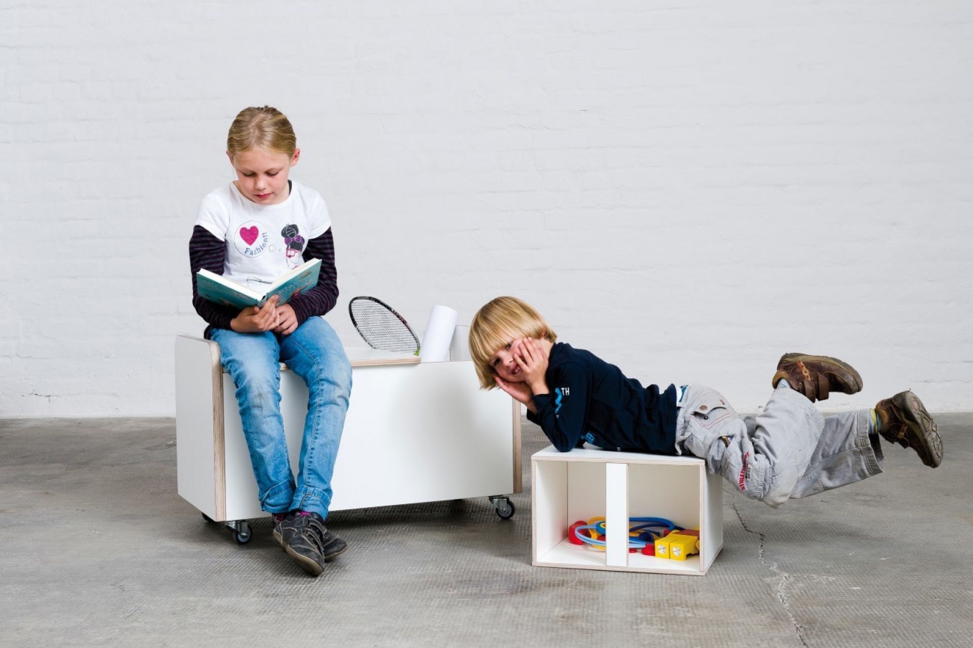 Zwei Kinder spielen mit der Growing Table Rollbox Truhe: Mädchen liest, Junge liegt darauf.