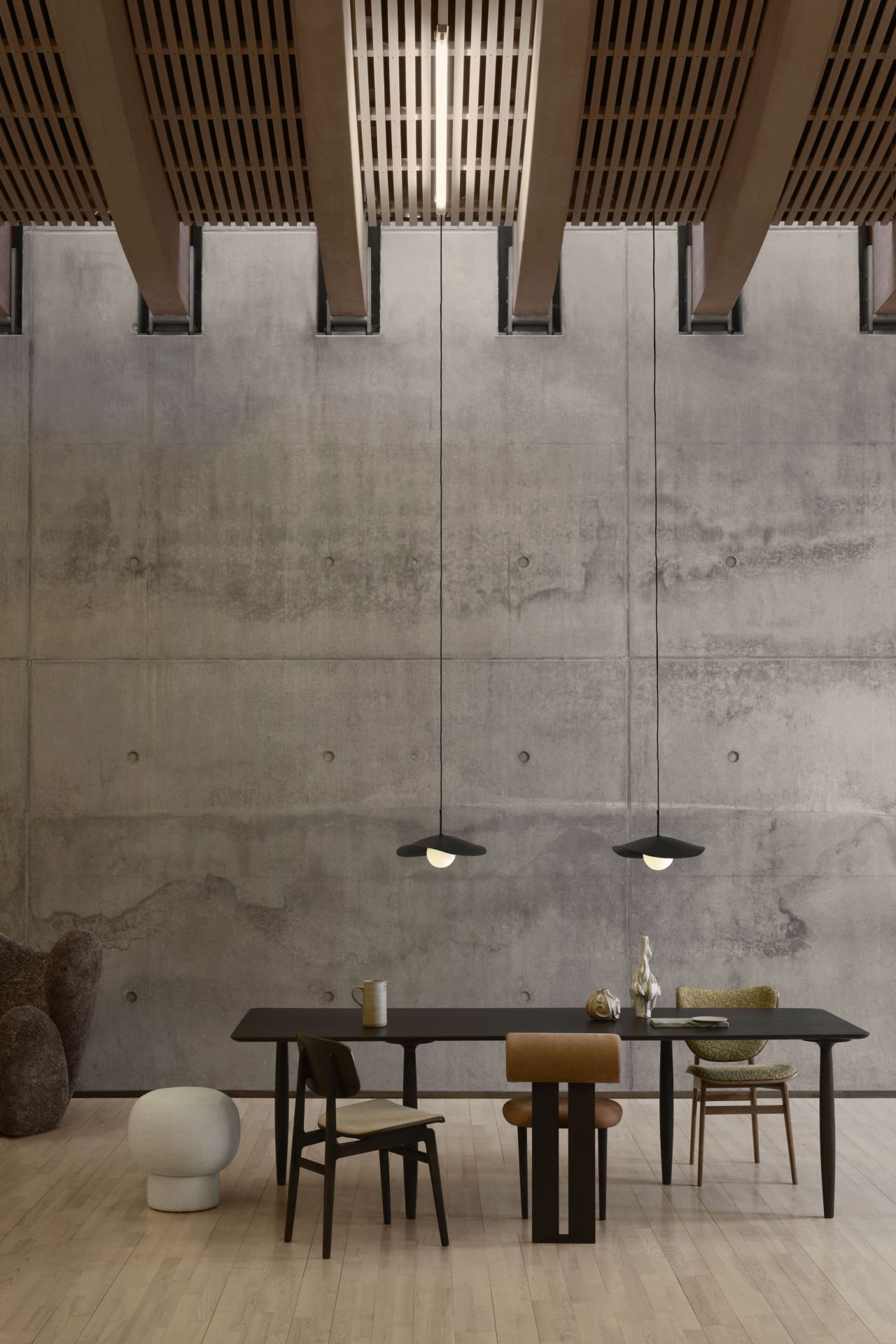 Fuji Pendelleuchte von Norr11 über Esstisch mit Stühlen, moderne Innenarchitektur mit Betonwand und Holzdecke.