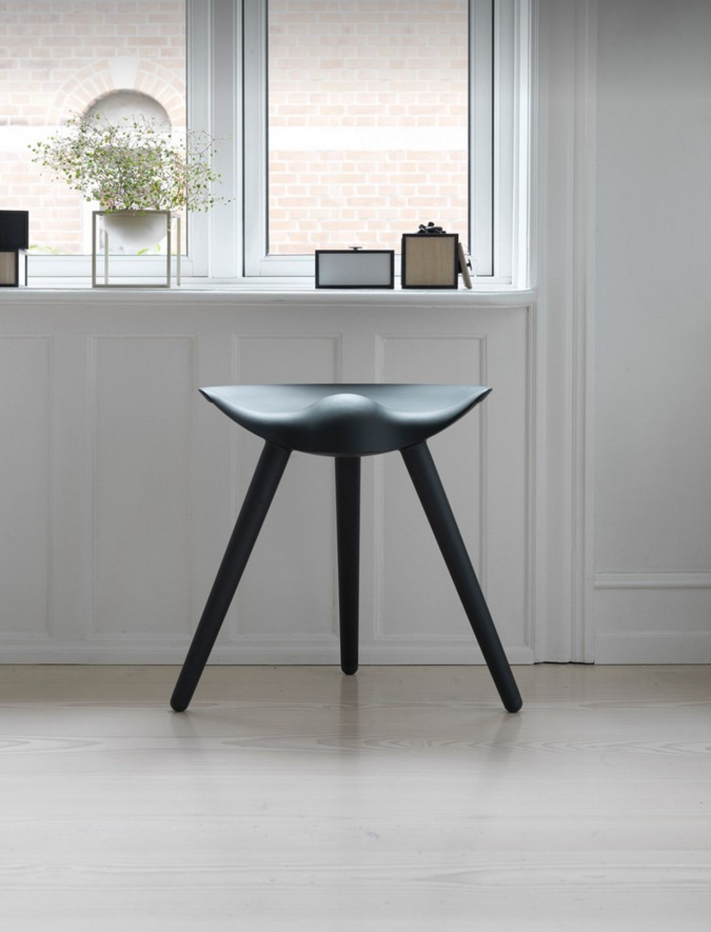 ML42 Hocker Audo aus schwarzem Holz vor einem Fenster, minimalistisches Design für modernes Wohnen.