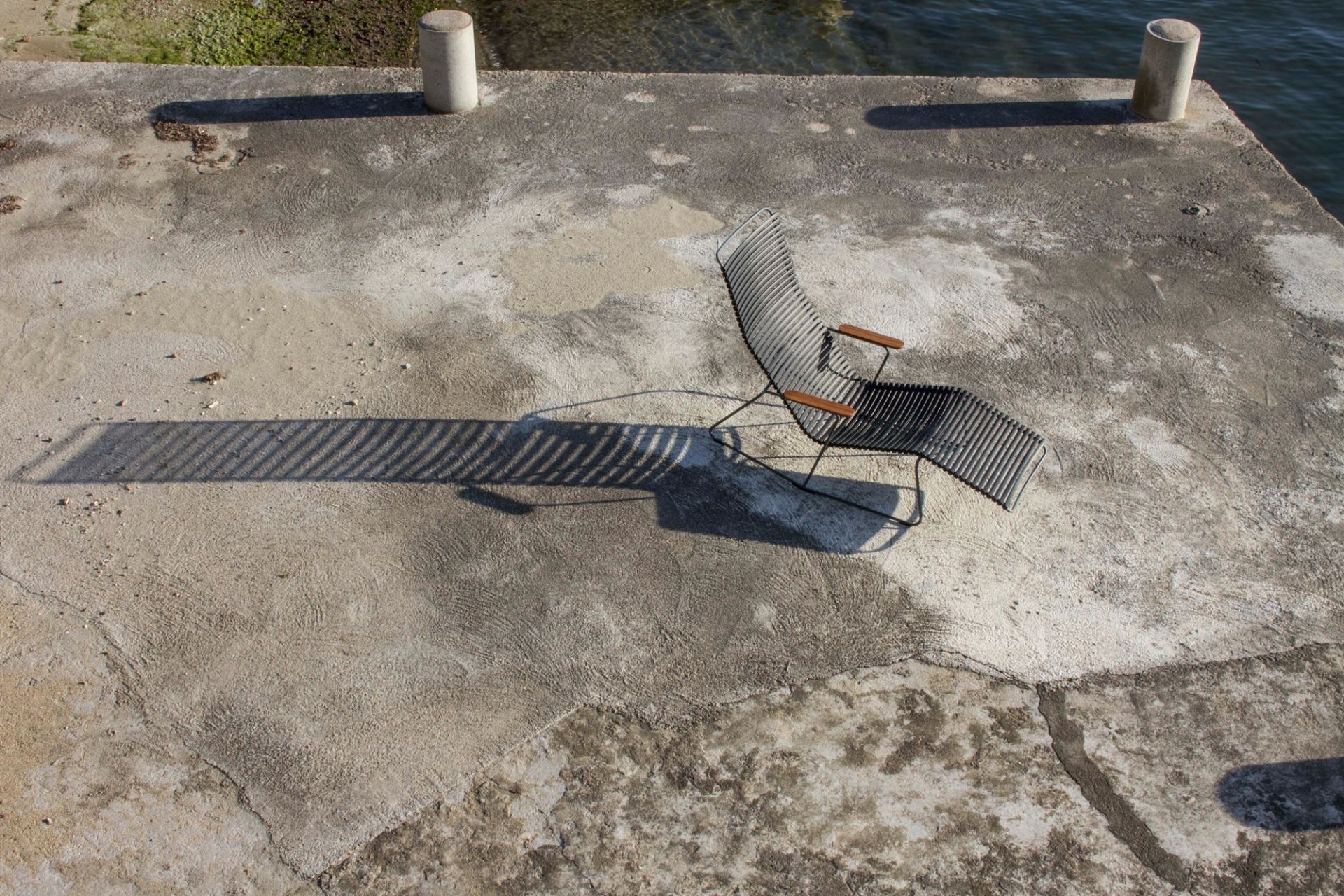 Click Sunrocker Sonnenliege in Dunkelgrau auf Steg mit Meerblick. Bequeme Outdoor Liege für Garten und Terrasse.