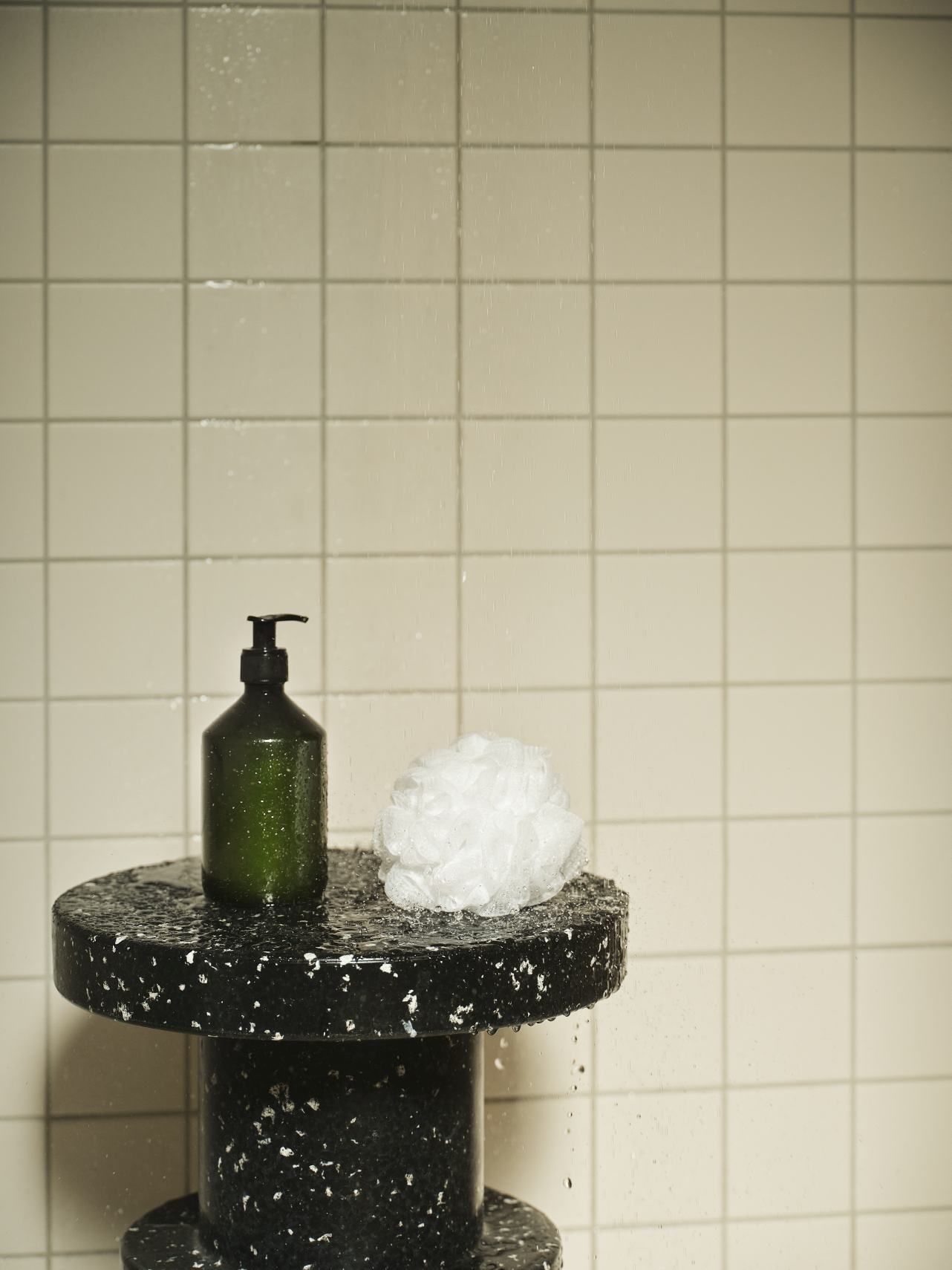 Normann Copenhagen Bit Stool Hocker in Schwarz-Weiß mit Seifenspender und Badeschwamm unter der Dusche.