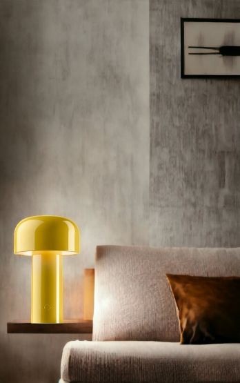Gelbe Bellhop Akku Tischleuchte von Flos auf einem Regal neben einem Sofa.
