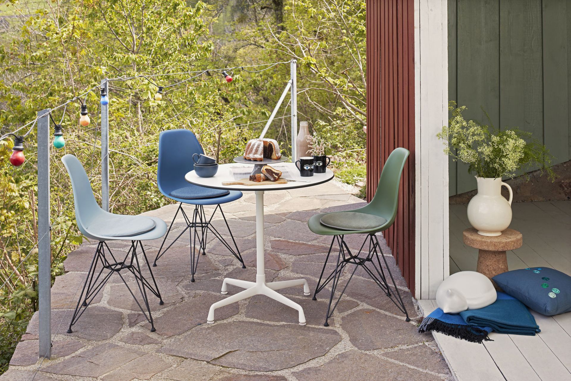 Drei Eames Plastic Side Chairs DSR von Vitra in Eisgrau, Blau und Grün auf Terrasse.