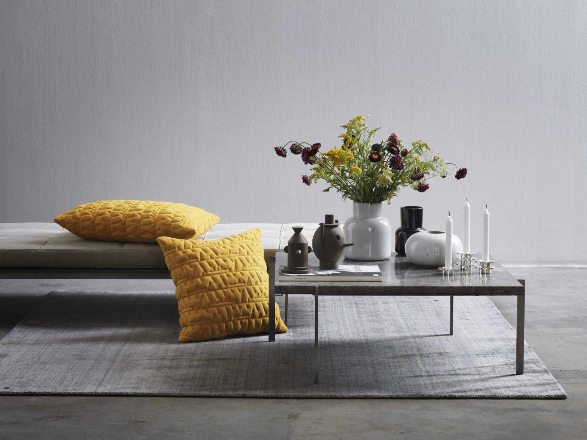 Helle Inneneinrichtung mit PK 80 Liege von Fritz Hansen und gelben Kissen auf einem grauen Teppich.