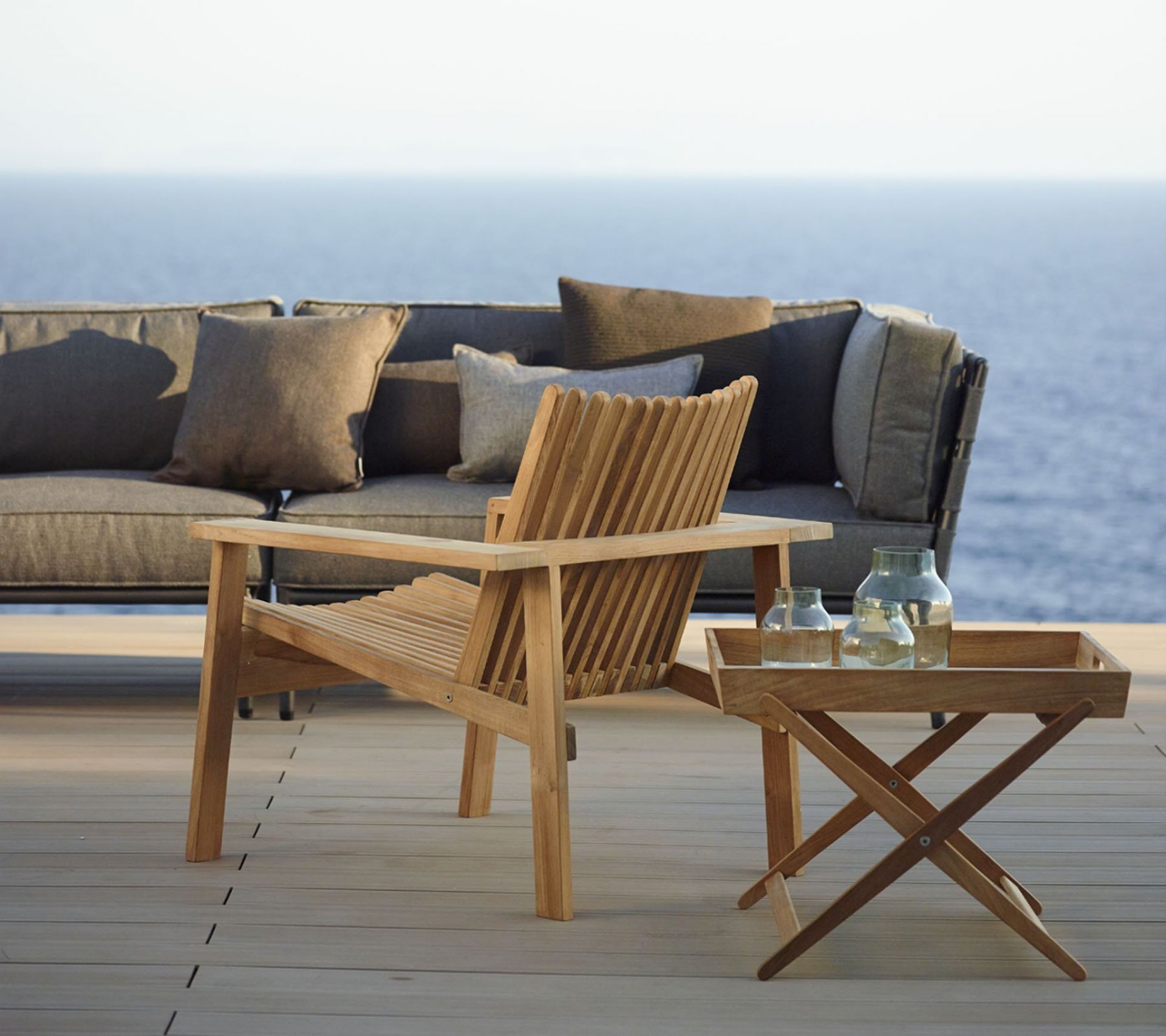 Amaze Outdoor Loungesessel von Cane-Line aus Teakholz mit Beistelltisch und Sofa im Hintergrund.