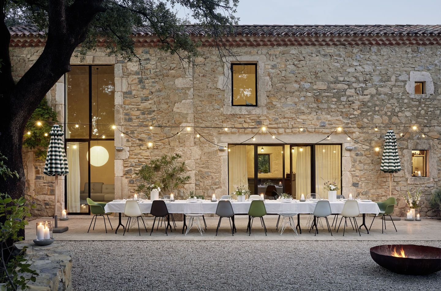 Esstisch im Freien mit Vitra Eames Plastic Side Chairs DSX, verschiedenen Farben, vor Steinhaus.