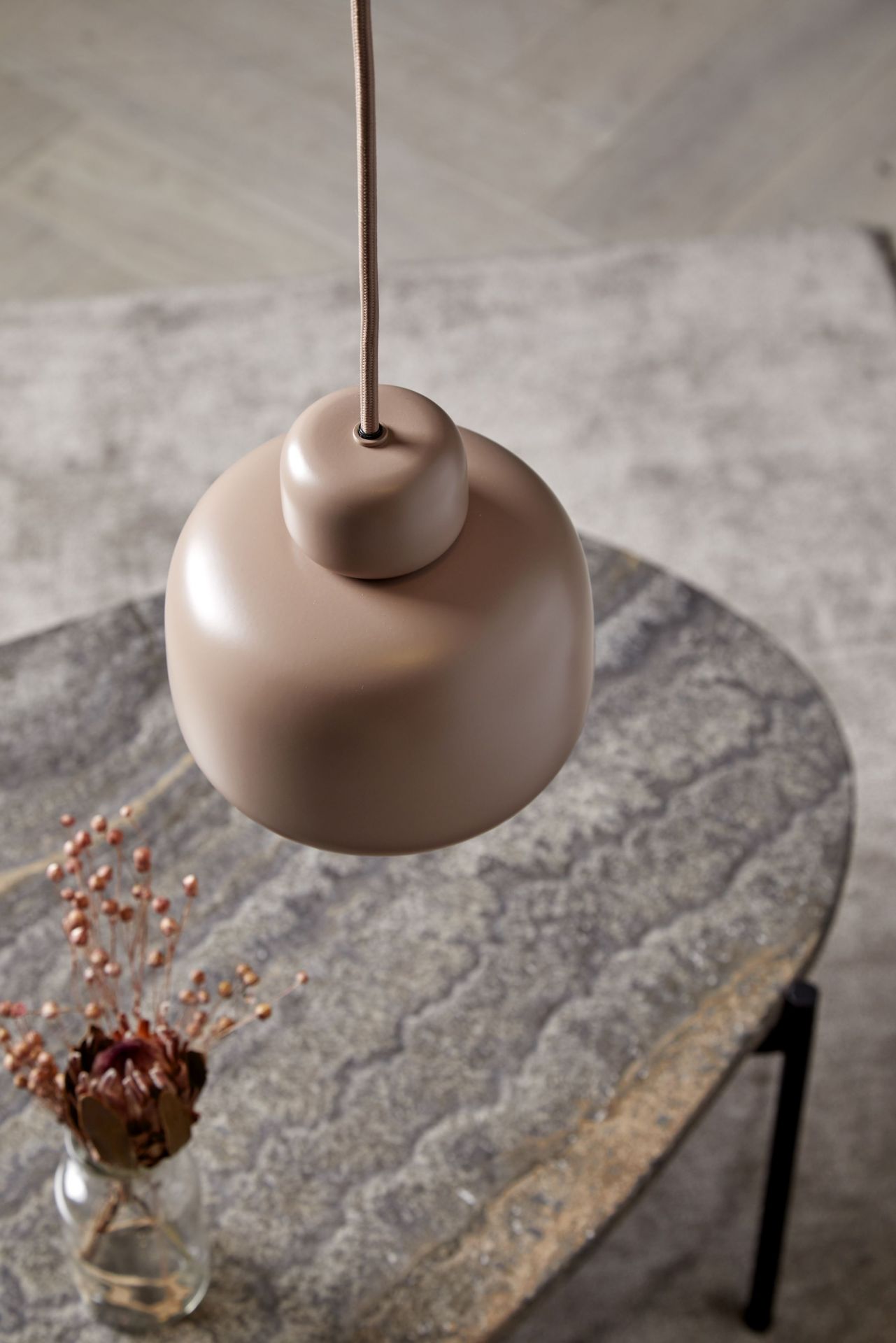 Nahaufnahme der kleinen Woud Stone Pendant Pendelleuchte in Beige, hängend über einem Steintisch.