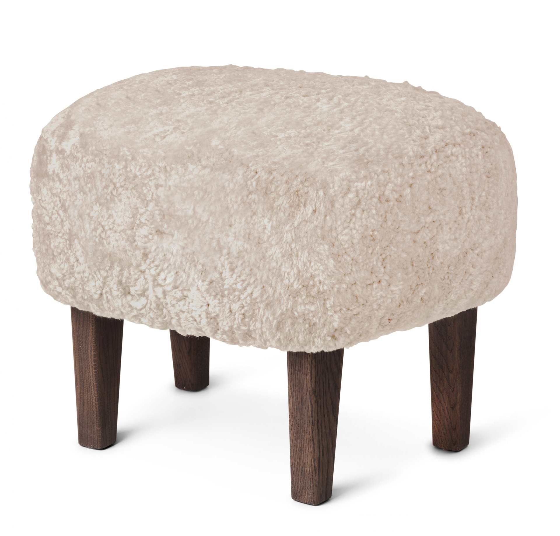 Ingeborg Ottoman von Audo, runder Hocker mit cremefarbenem Schaffellbezug und dunklen Holzfüßen.