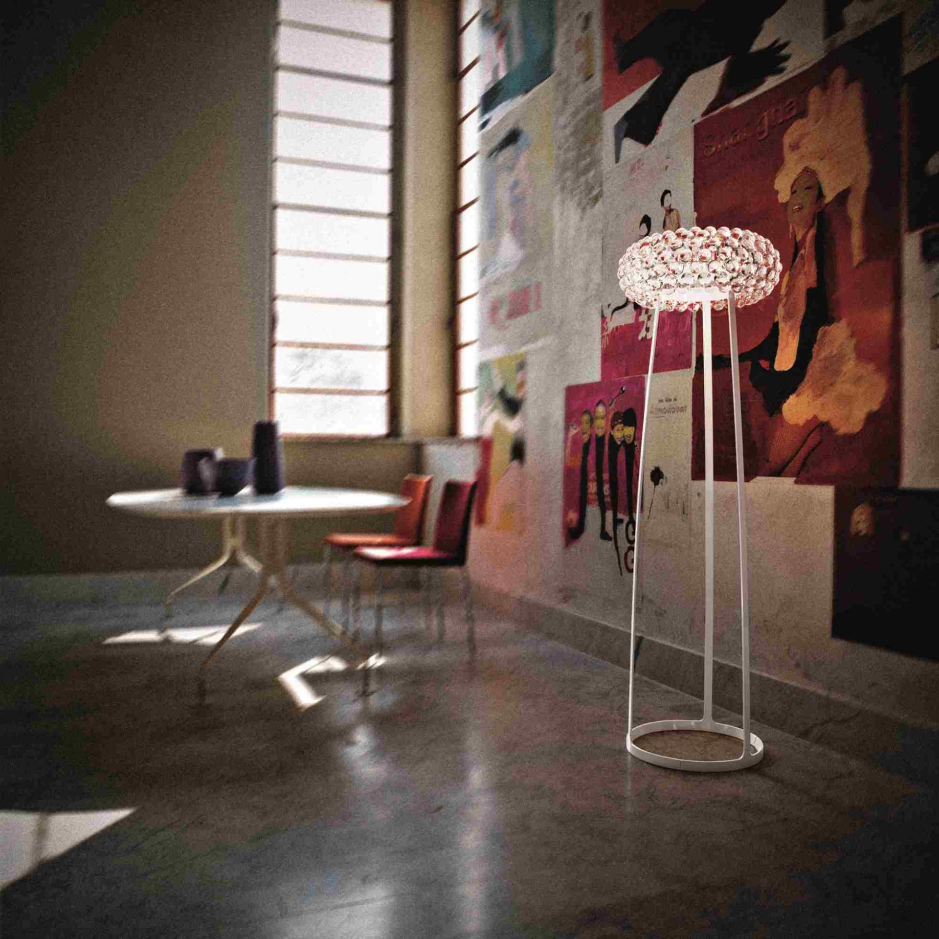 Moderne Stehlampe mit Kristall-Schirm und weißem Metallgestell in einem Raum mit Kunstpostern.