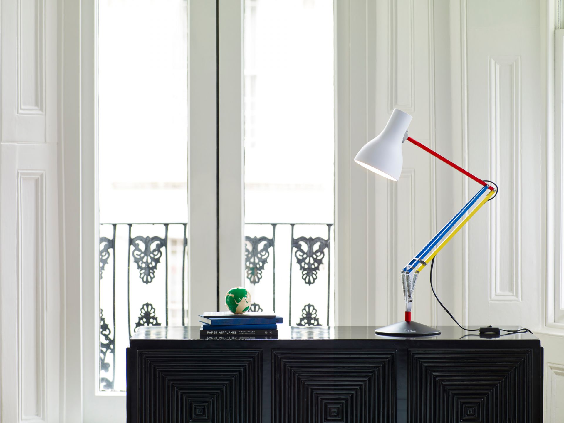 Anglepoise Type 75 Mini Paul Smith Edition Tischleuchte auf schwarzem Sideboard vor weißer Flügeltür.