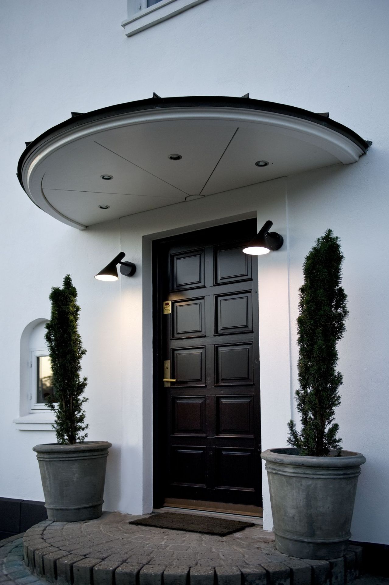 AJ 50 Wandleuchte von Louis Poulsen in Schwarz an einer weißen Hauswand neben einer Haustür.