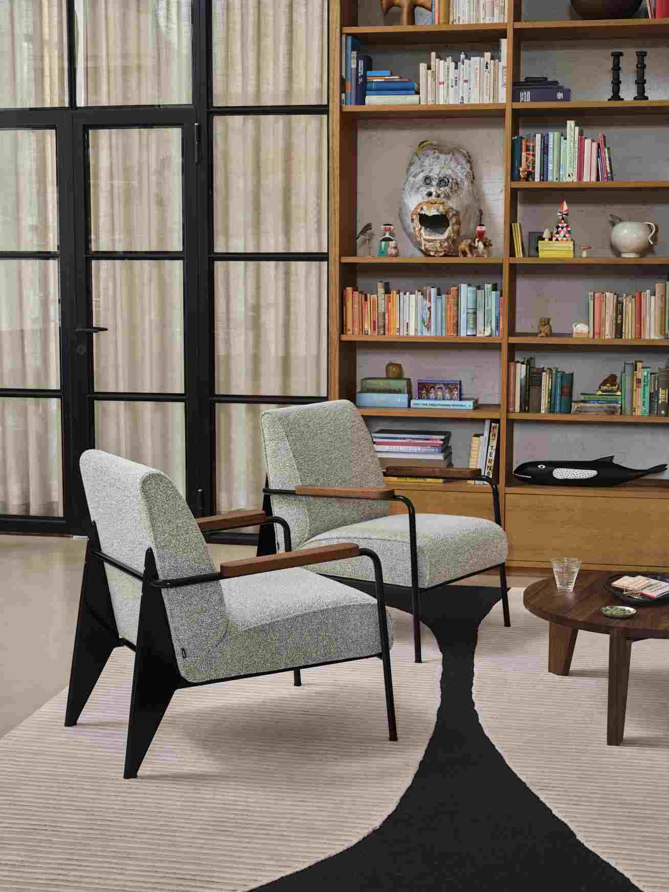 Zwei graue Sessel mit Holzarmlehnen und eine Vitra Eames House Whale Skulptur im Hintergrund auf einem Bücherregal.