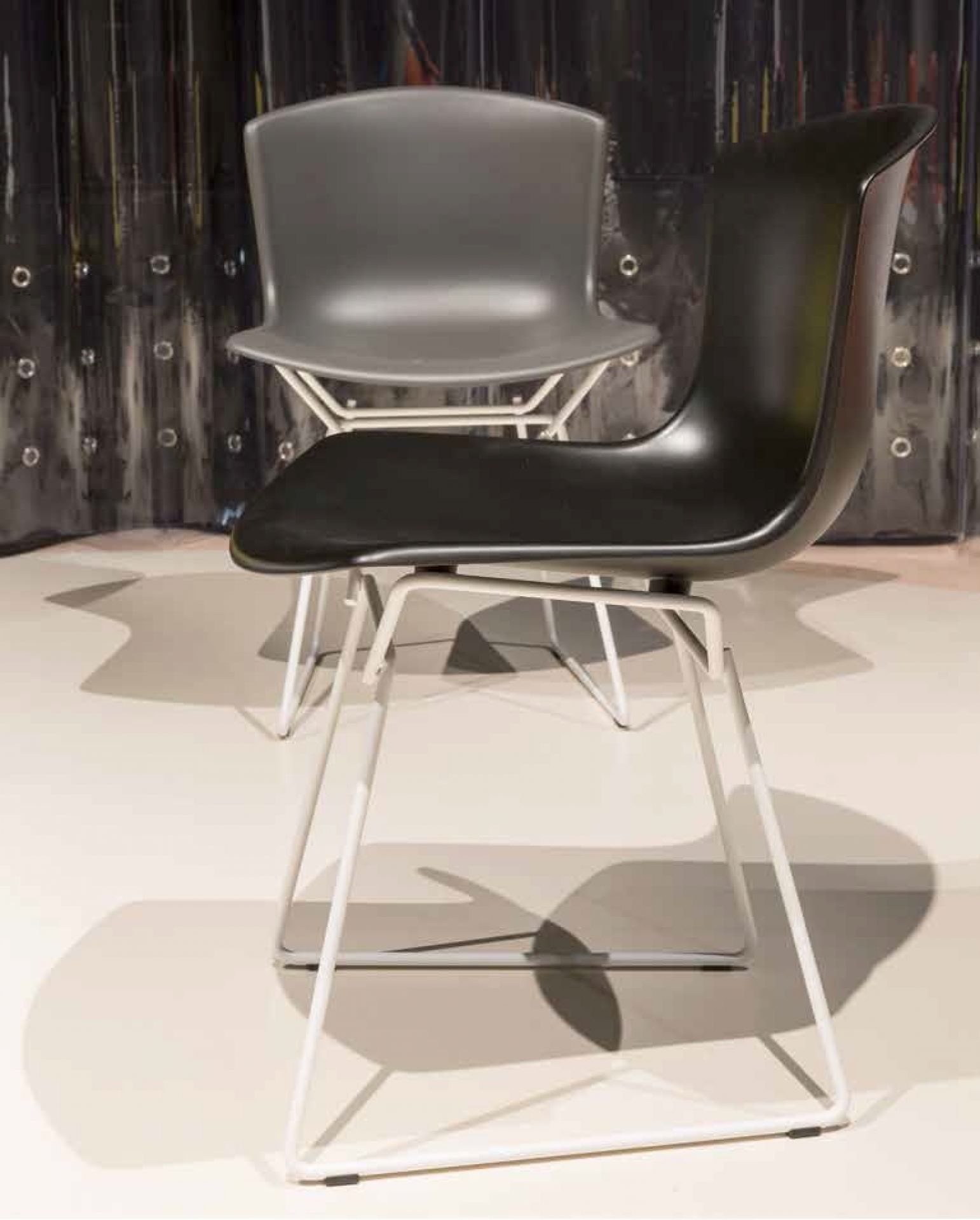Schwarzer Bertoia Stuhl mit weißem Chromgestell und ein grauer Bertoia Stuhl im Hintergrund.