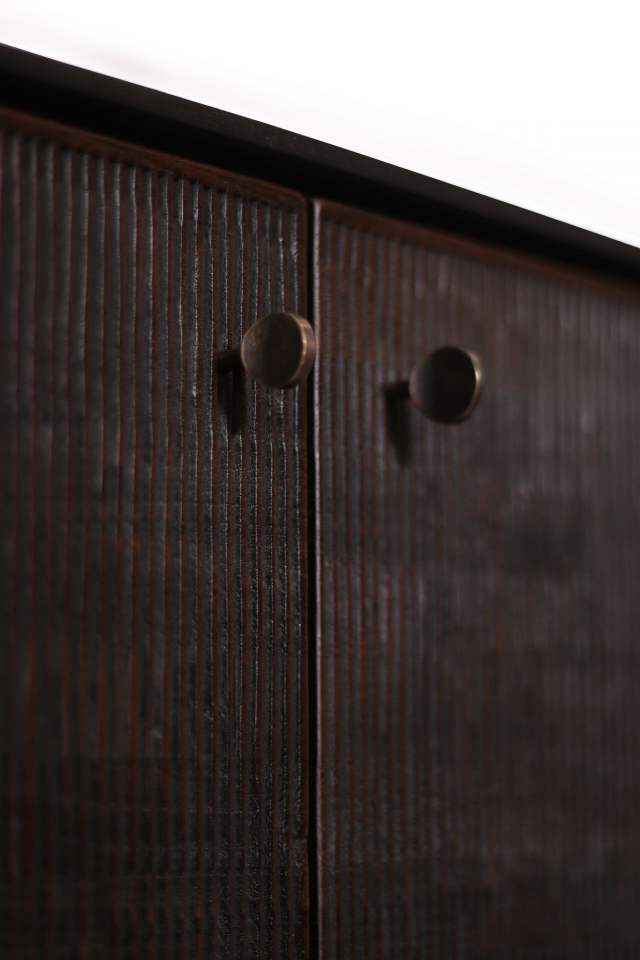 Detailaufnahme der Ethnicraft Teak Grooves Anrichte mit dunklem Holz und zwei runden bronzefarbenen Griffen.
