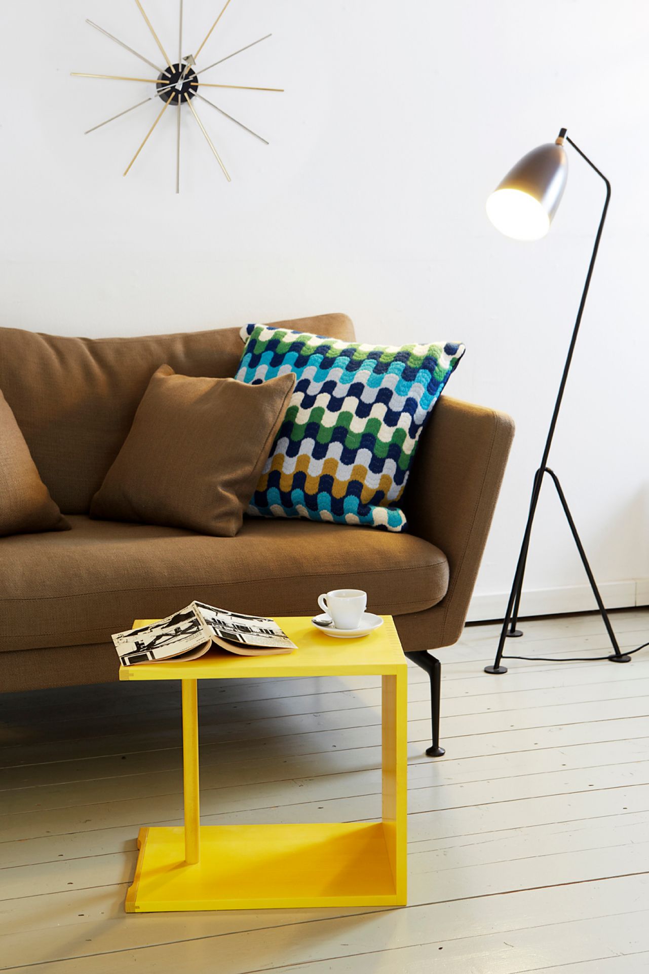 Gelber Ulmer Hocker von Max Bill neben braunem Sofa mit Kaffeetasse und Magazin.