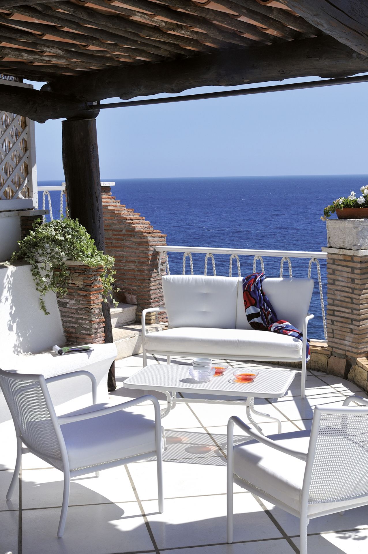 Weißes Athena 2-Sitzer Sofa von Emu auf einer Terrasse mit Meerblick. Outdoor Möbel Set.