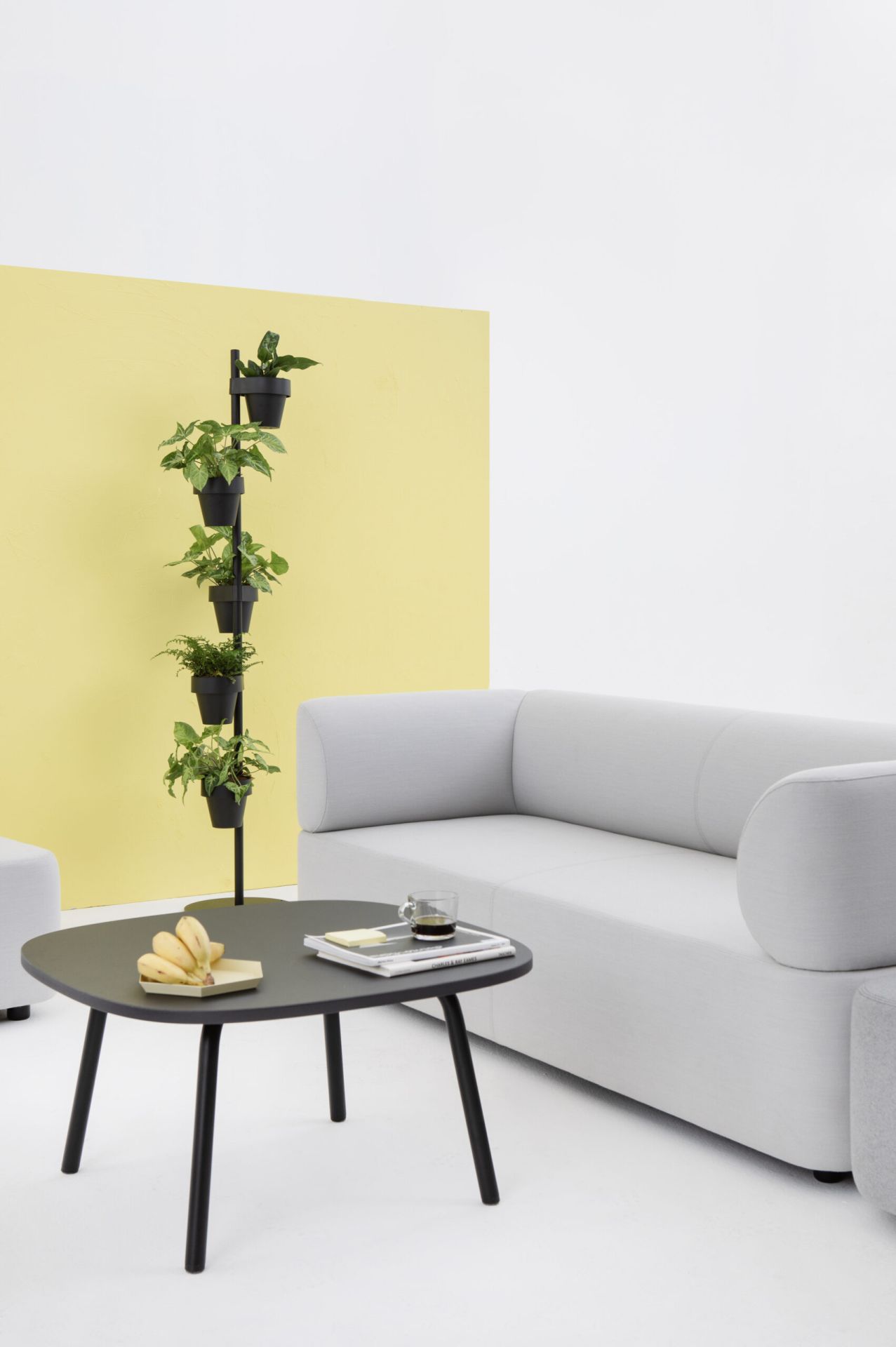 Helles Mezza Sitzelement Sofa von Cascando mit schwarzem Tisch, Pflanzenständer und gelbem Hintergrund.