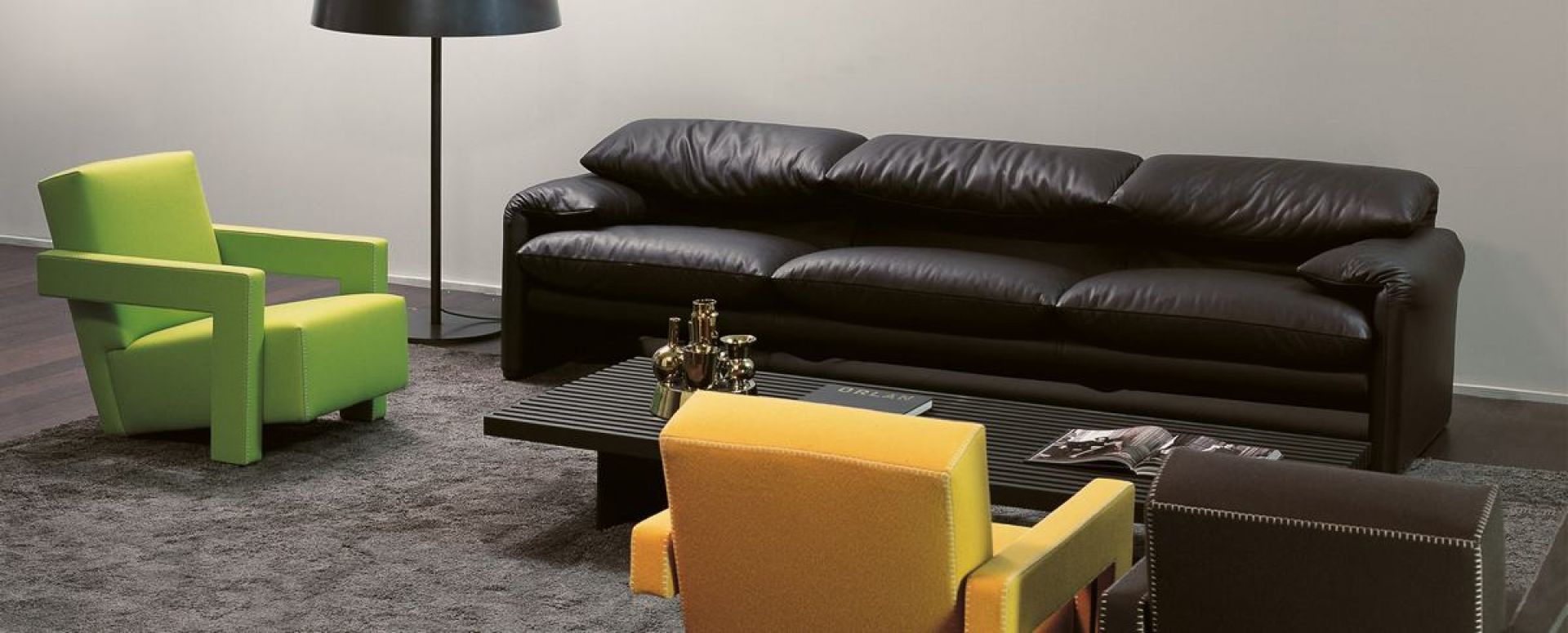 Schwarzes Cassina Maralunga Ledersofa, Dreisitzer, mit farbigen Sesseln und Couchtisch auf grauem Teppich.