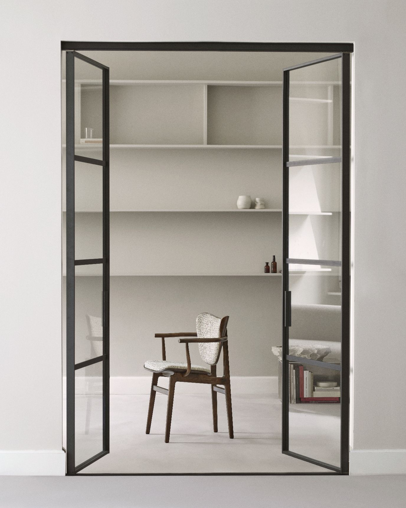NORR11 Elephant Dining Armchair mit Armlehnen, Holzgestell und Stoffbezug, vor Bücherregal und Glastüren.
