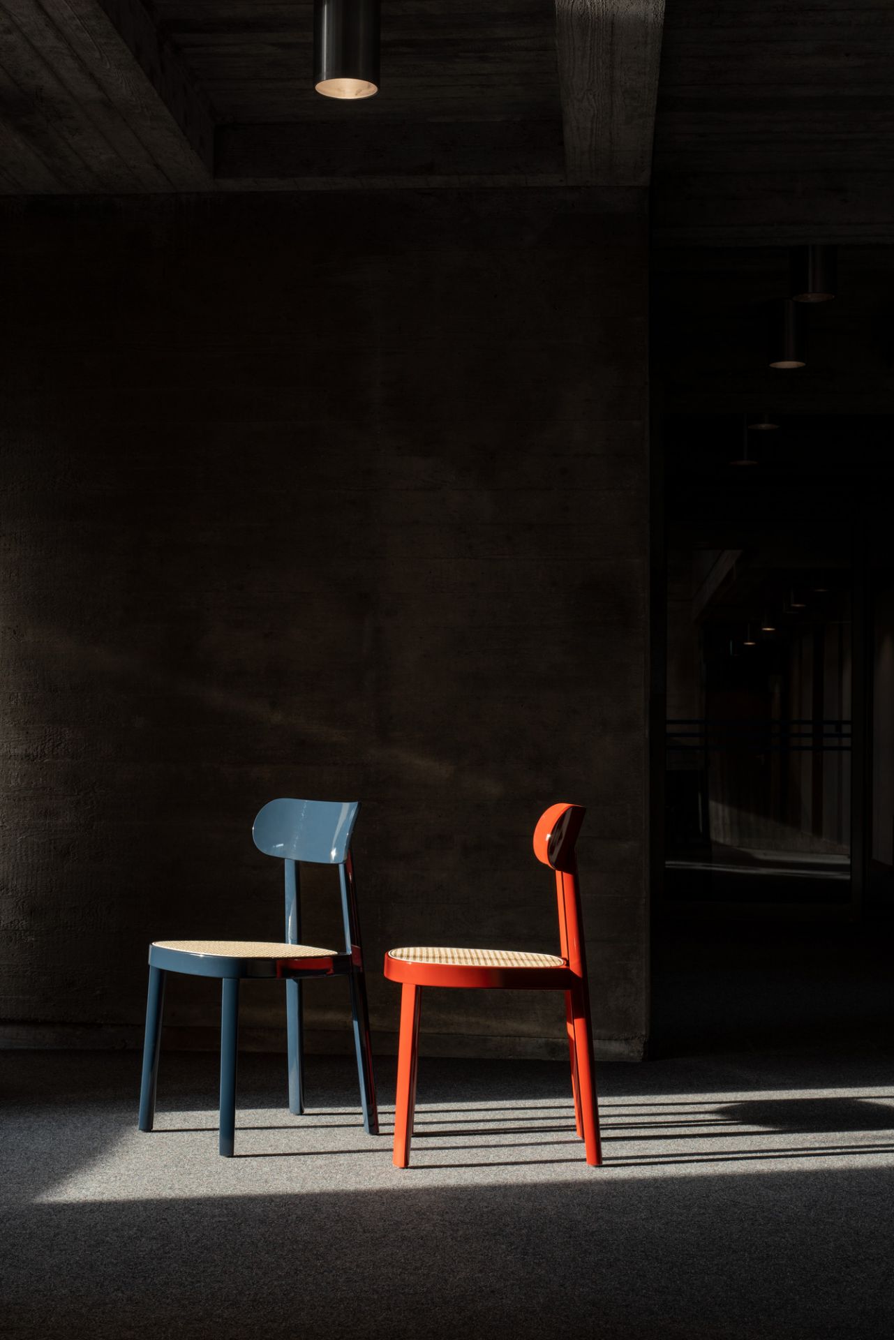Blauer und roter Holzstuhl Thonet 118 mit Wiener Geflecht Sitzfläche vor dunklem Hintergrund.