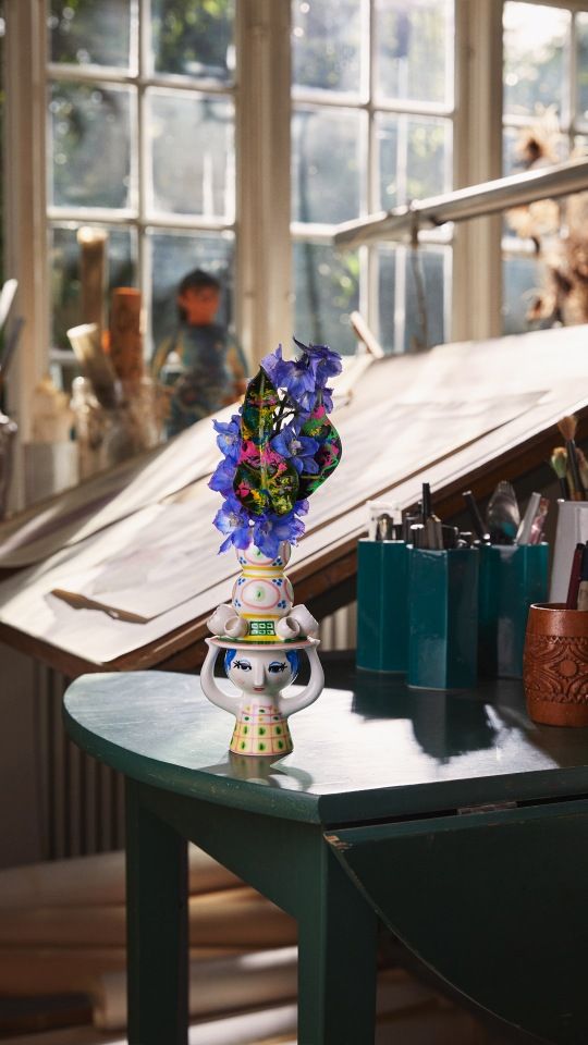 Lady with Hat Kerzenständer von Bjorn Wiinblad, dekoriert mit blauen Blumen, auf einem grünen Tisch.
