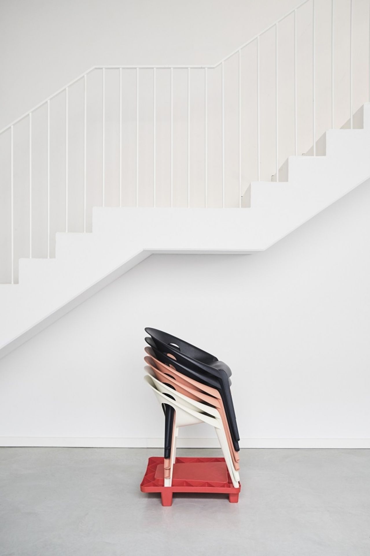 Gestapelte Bell Chairs Indoor/Outdoor Stühle von Magis in Schwarz, Beige und Weiß auf rotem Untergestell.