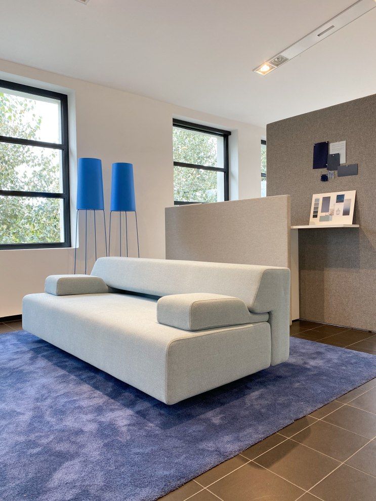 Helles Cosma Schlafsofa mit Armlehnen auf blauem Teppich, modernes Design für Wohnzimmer und Gästezimmer.