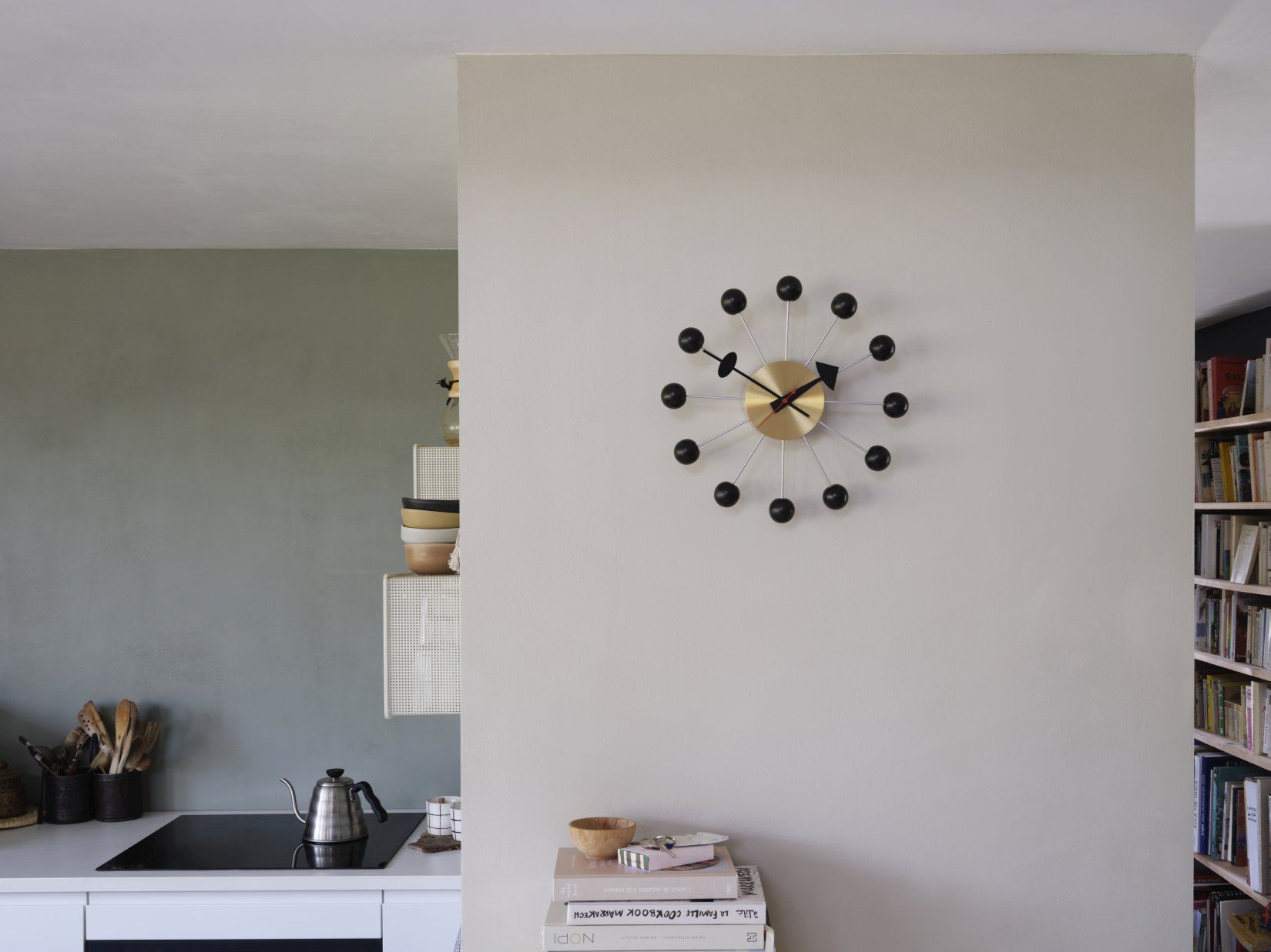Moderne Wanduhr im Atomic Design mit goldenem Zifferblatt und schwarzen Kugeln im Küchenambiente.