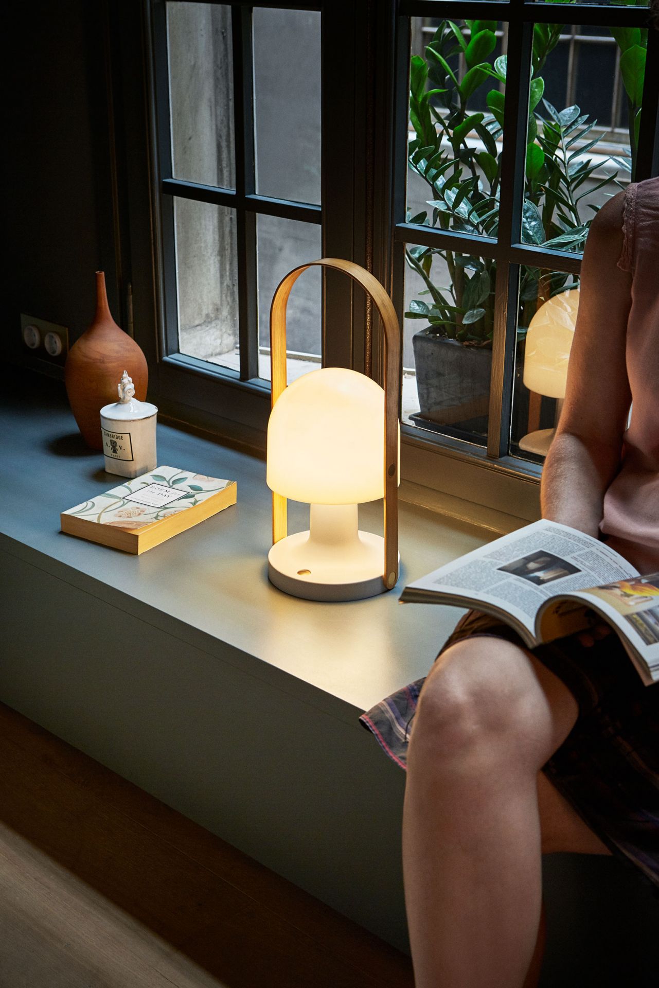 FollowMe Plus Akkuleuchte von Marset als Tischleuchte am Fenster, warmes Licht beim Lesen.