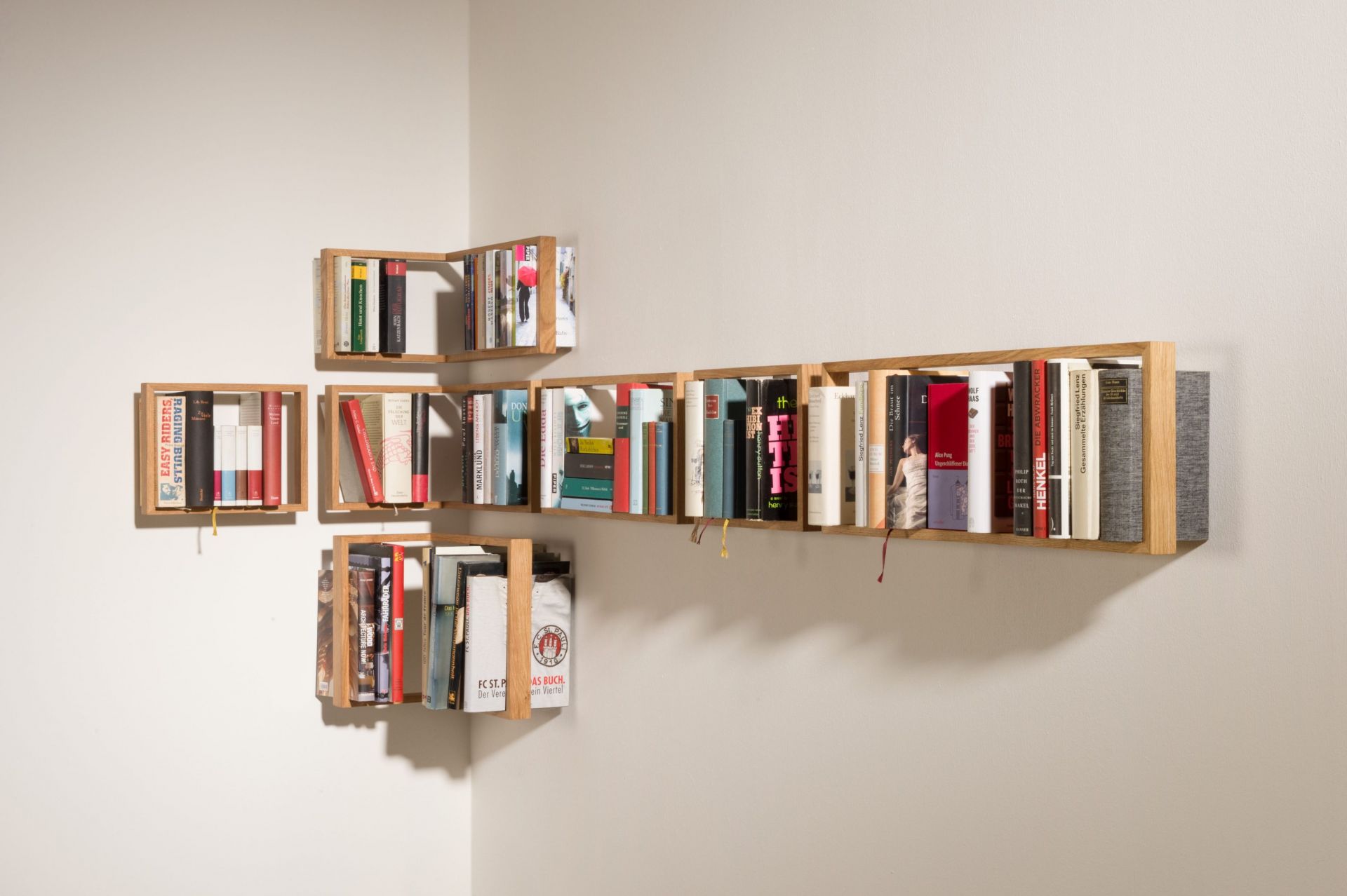 Wandmontiertes Regal b Eiche, bestehend aus mehreren kleinen Holzregalen, gefüllt mit Büchern, modernes Design, Unikat.