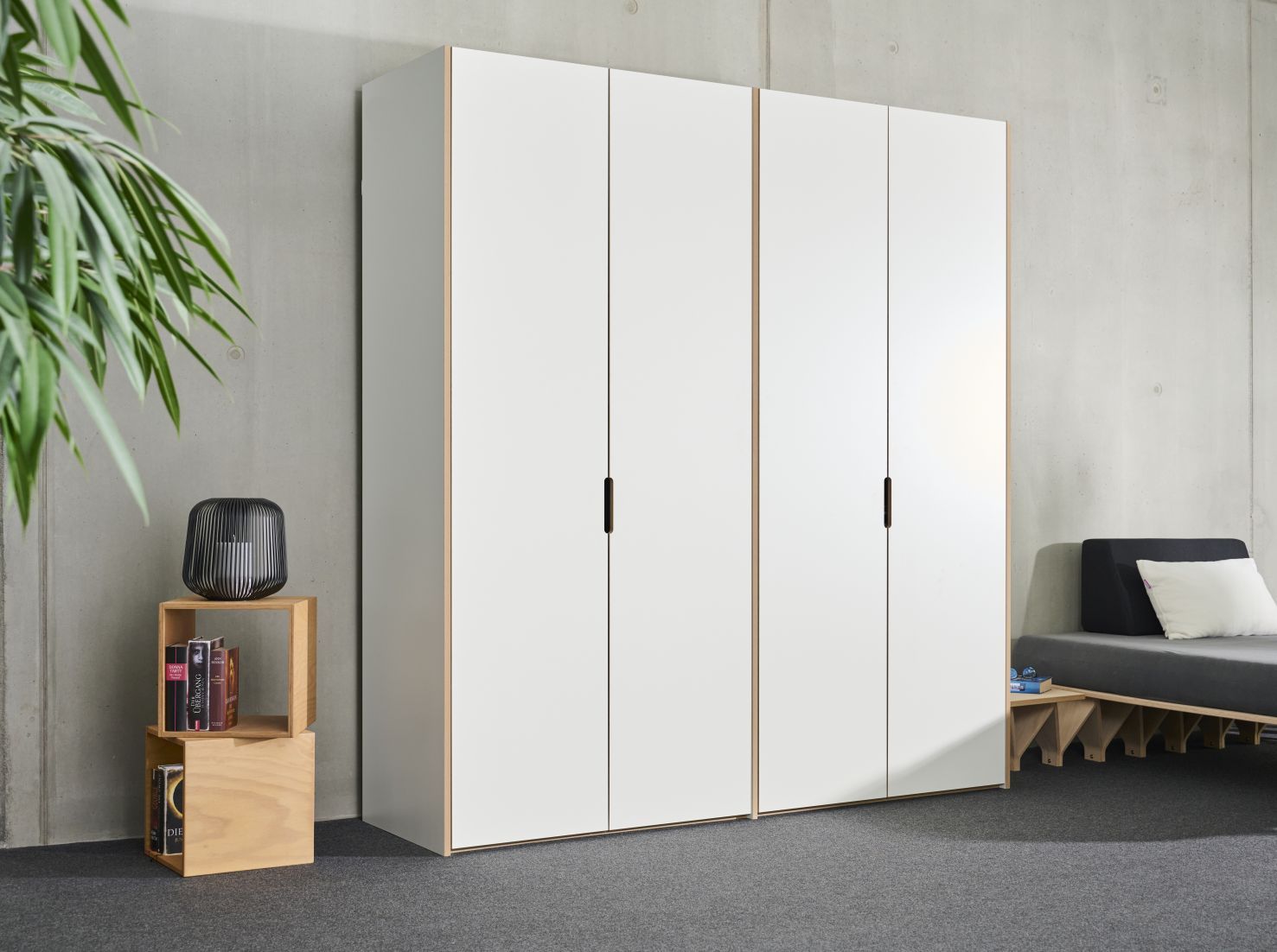 Tojo Schrank Anbaumodul mit vier weißen Türen und schmalen, senkrechten Griffen vor grauer Wand.