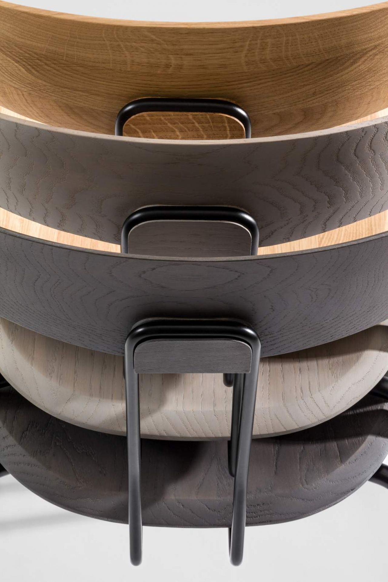 Detailaufnahme von gestapelten Okito Chair Stühlen der Marke Zeitraum, verschiedene Holzfarben und schwarze Metallbeine.