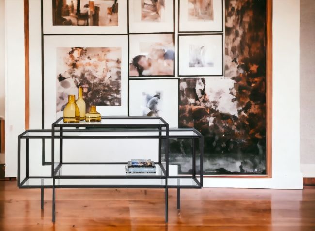 Tangled Kabinettschrank Sideboard Spectrum mit Glasablagen und schwarzem Metallgestell vor einer Bilderwand.