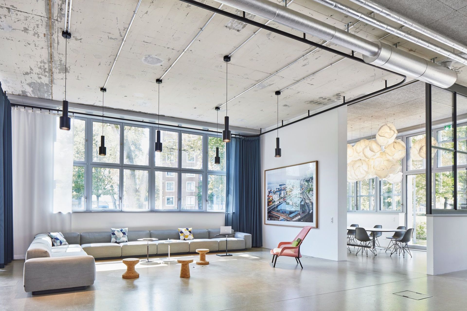 Heller, moderner Büroraum mit großem Fenster, grauer Couch, Korkhockern und einem Slow Chair Sessel von Vitra.