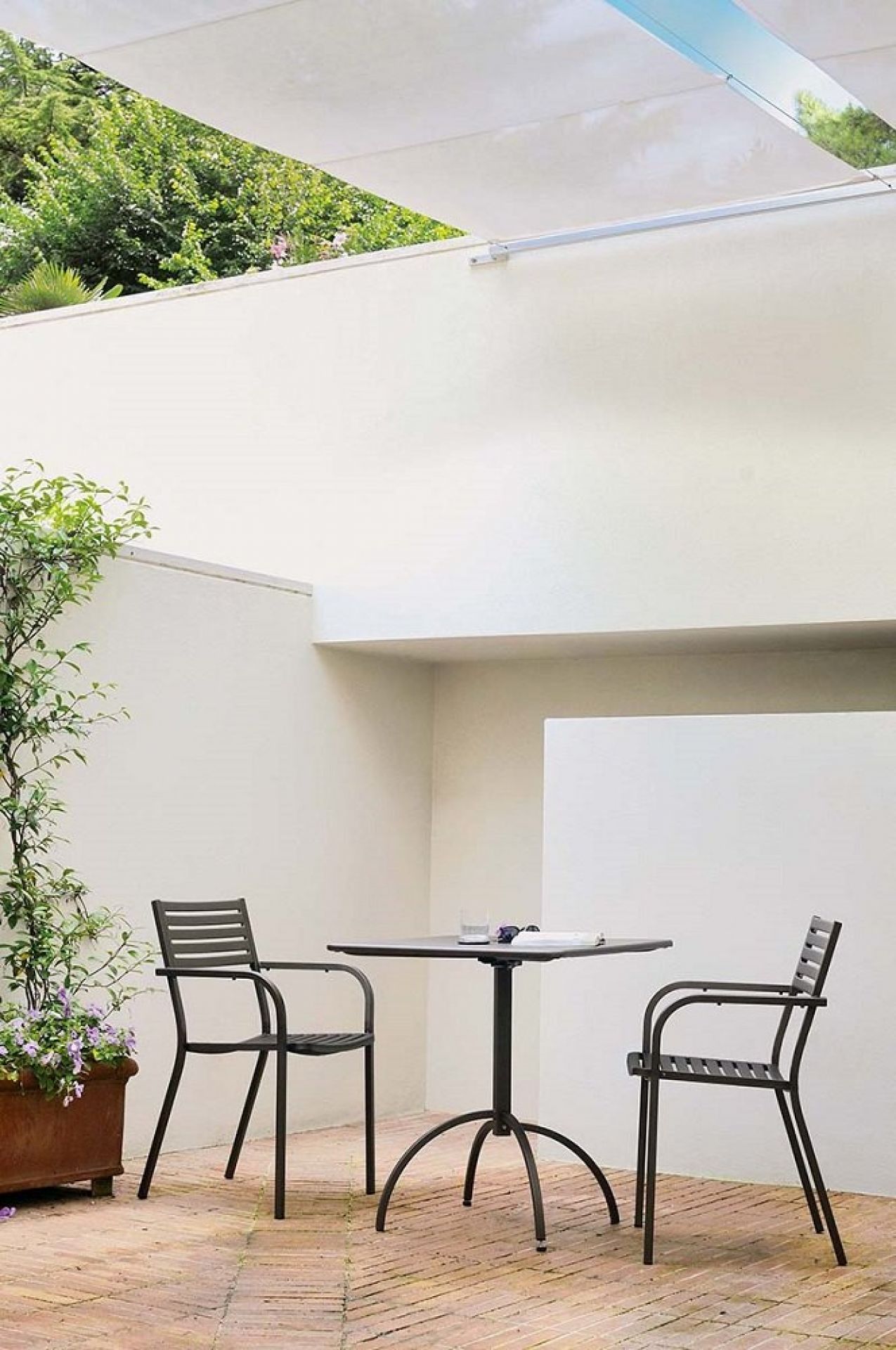 Schwarzer Emu Armlehnstuhl Segno im Außenbereich mit Tisch und Pflanze, Gartenmöbel für Terrasse.