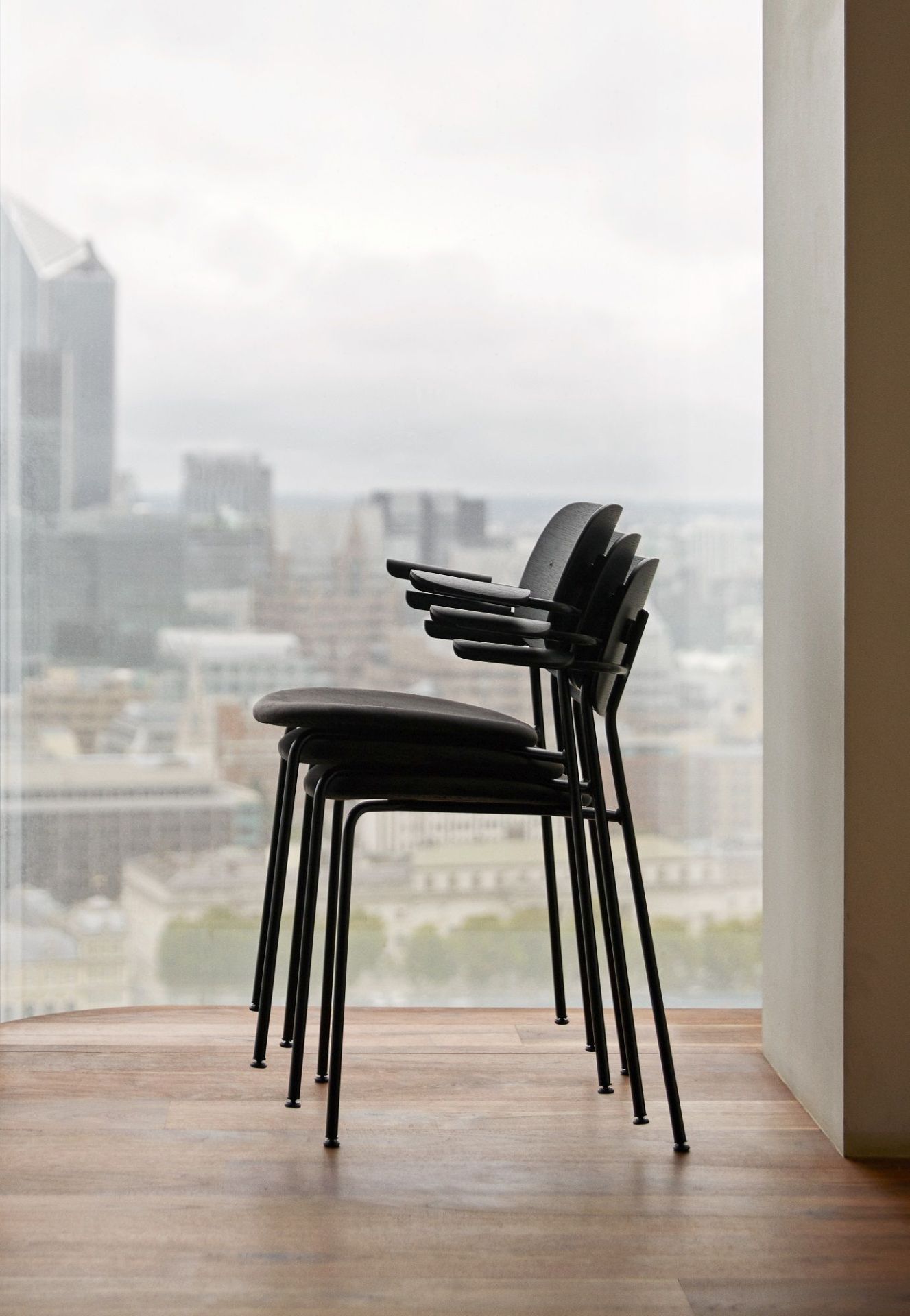 Stapel aus schwarzen Co Dining Chair Stühlen von Audo Copenhagen vor einem Fenster mit Stadtblick.